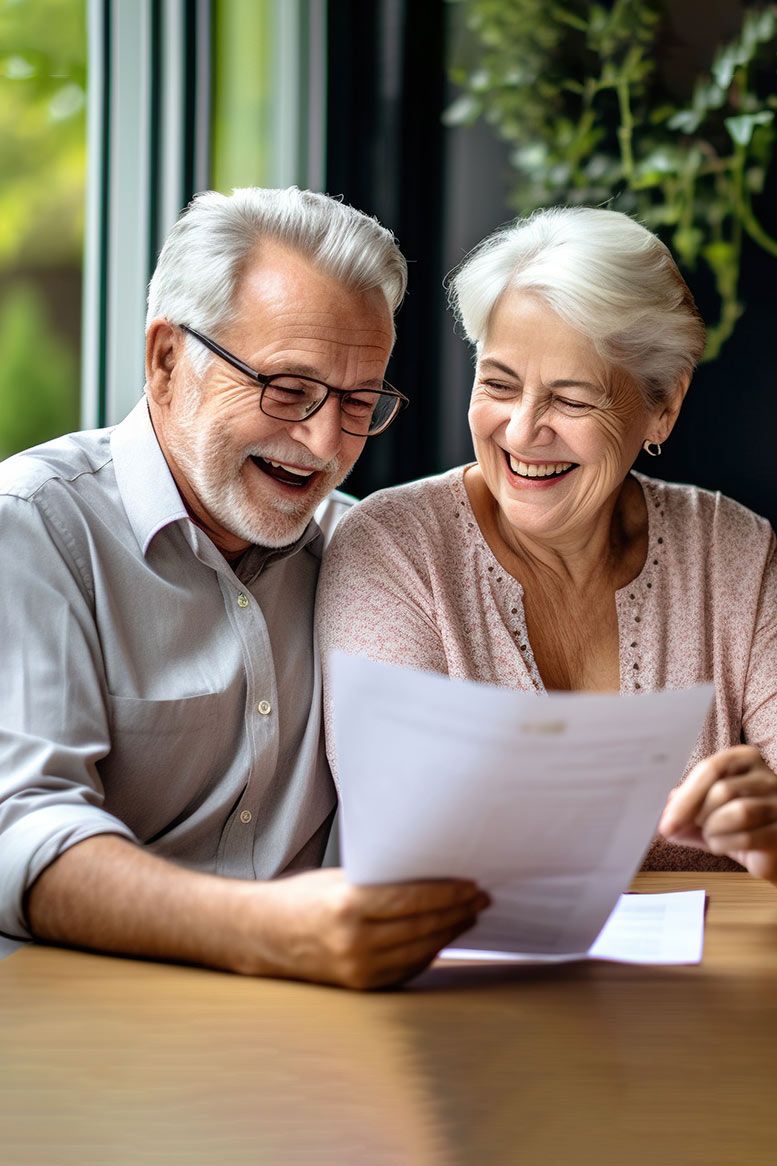 An elderly couple is sitting at a table looking at a piece of paper.