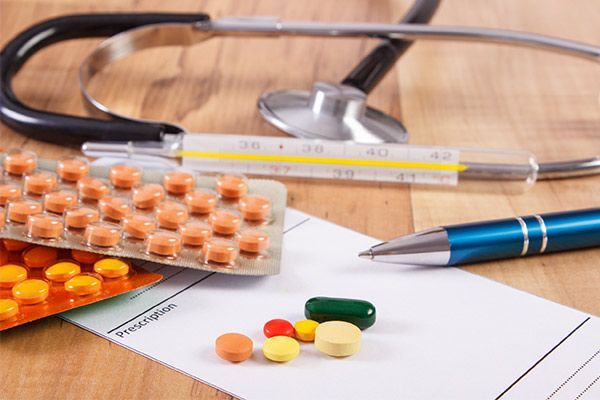 A stethoscope , thermometer , pills and a pen are on a wooden table.