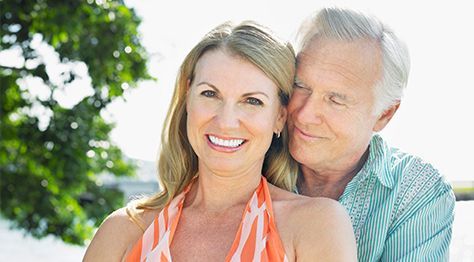 A man and a woman are posing for a picture . the woman is smiling and the man is hugging her.