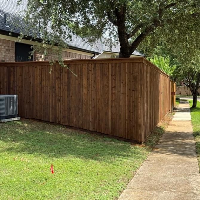 Black metal fence with hedges and green grass bordering modern townhouses.