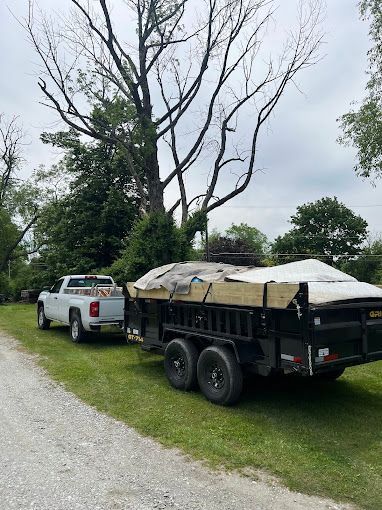 A white truck is towing a dump trailer with a tree in the background.