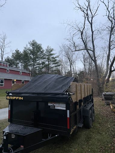A dumpster trailer is parked in a yard with trees in the background.