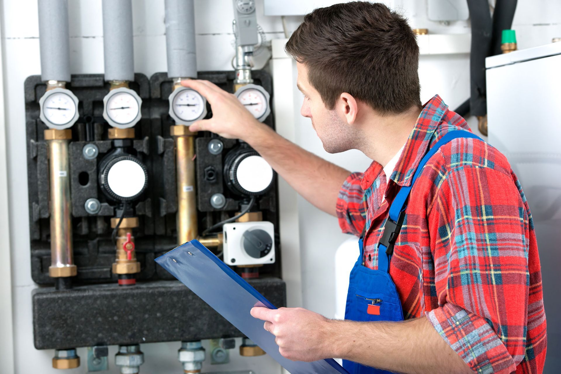 A man is working on a boiler and holding a clipboard.
