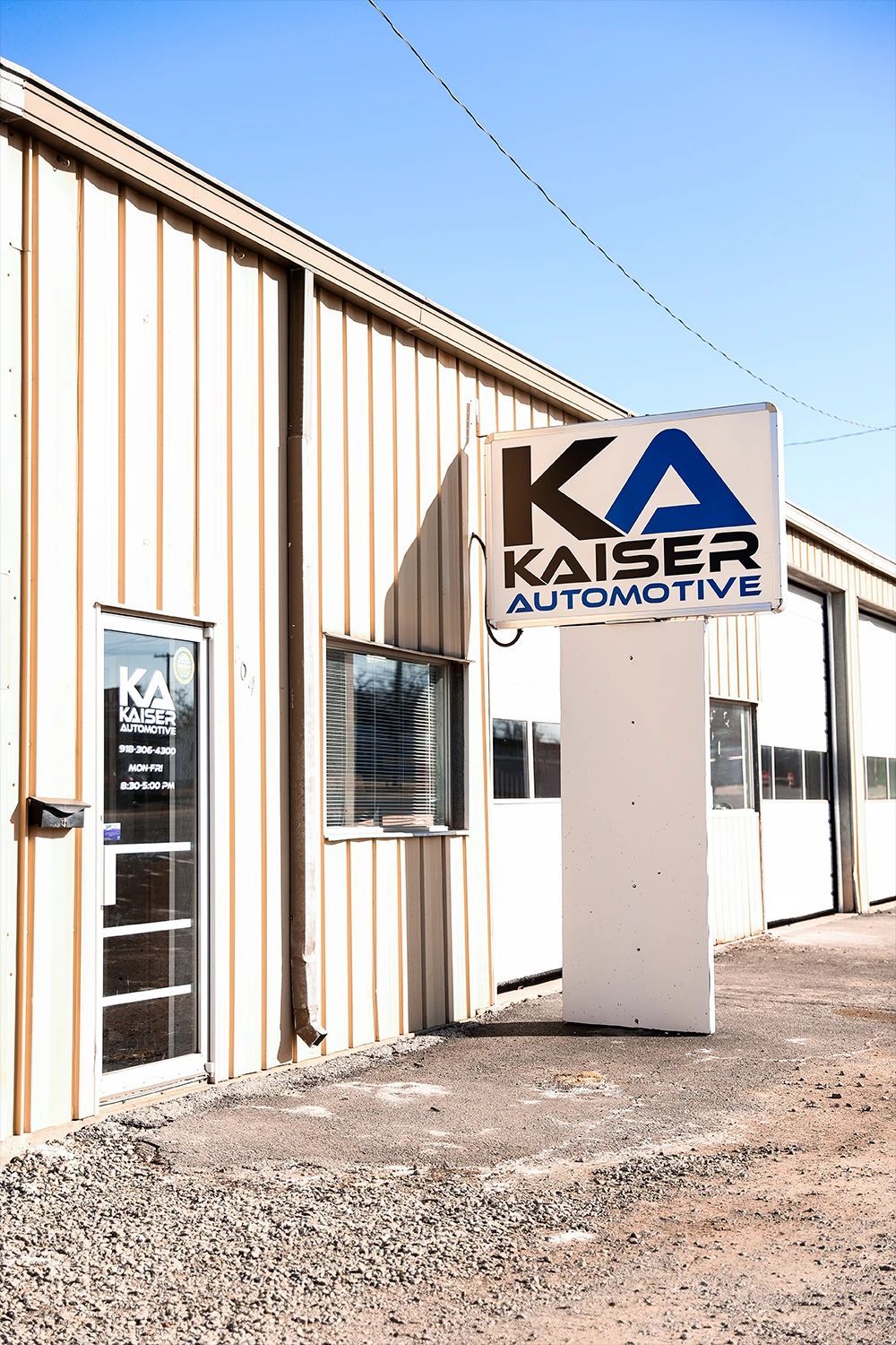 Kaiser Automotive building with a sign on a sunny day. Light brown exterior with garage doors | Kaiser Automotive