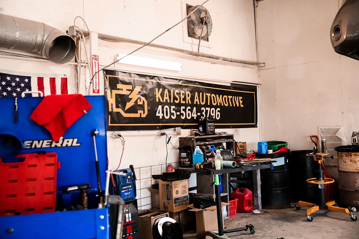 Inside a Kaiser Automotive garage, tools and equipment are displayed, along with an American flag and a banner with a phone number | Kaiser Automotive