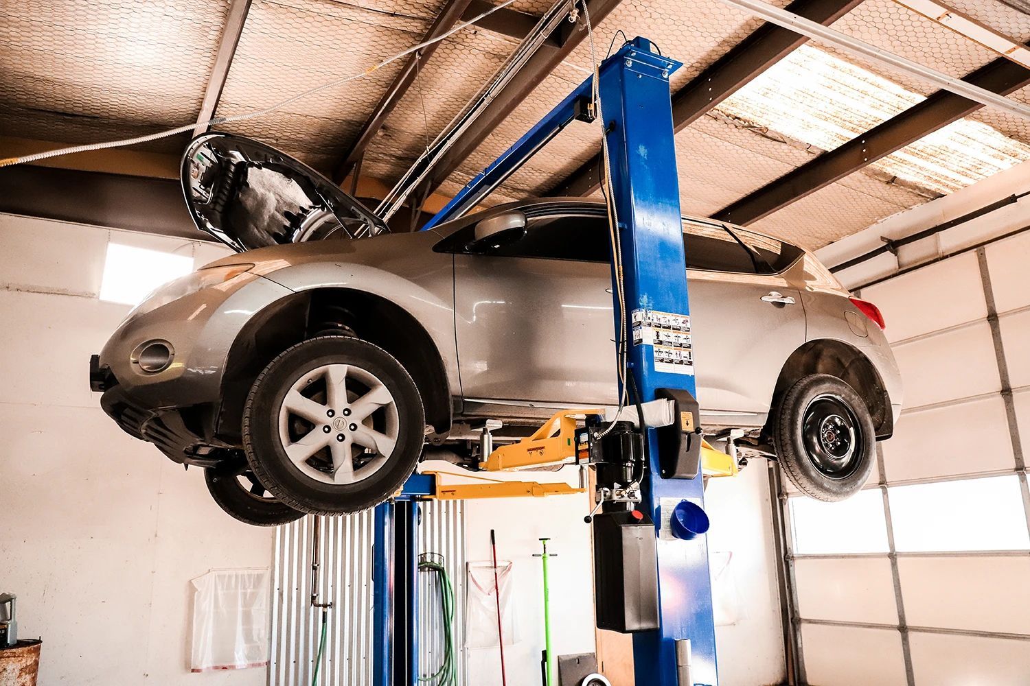 Silver car raised on a blue lift in a garage, hood open | Kaiser Automotive