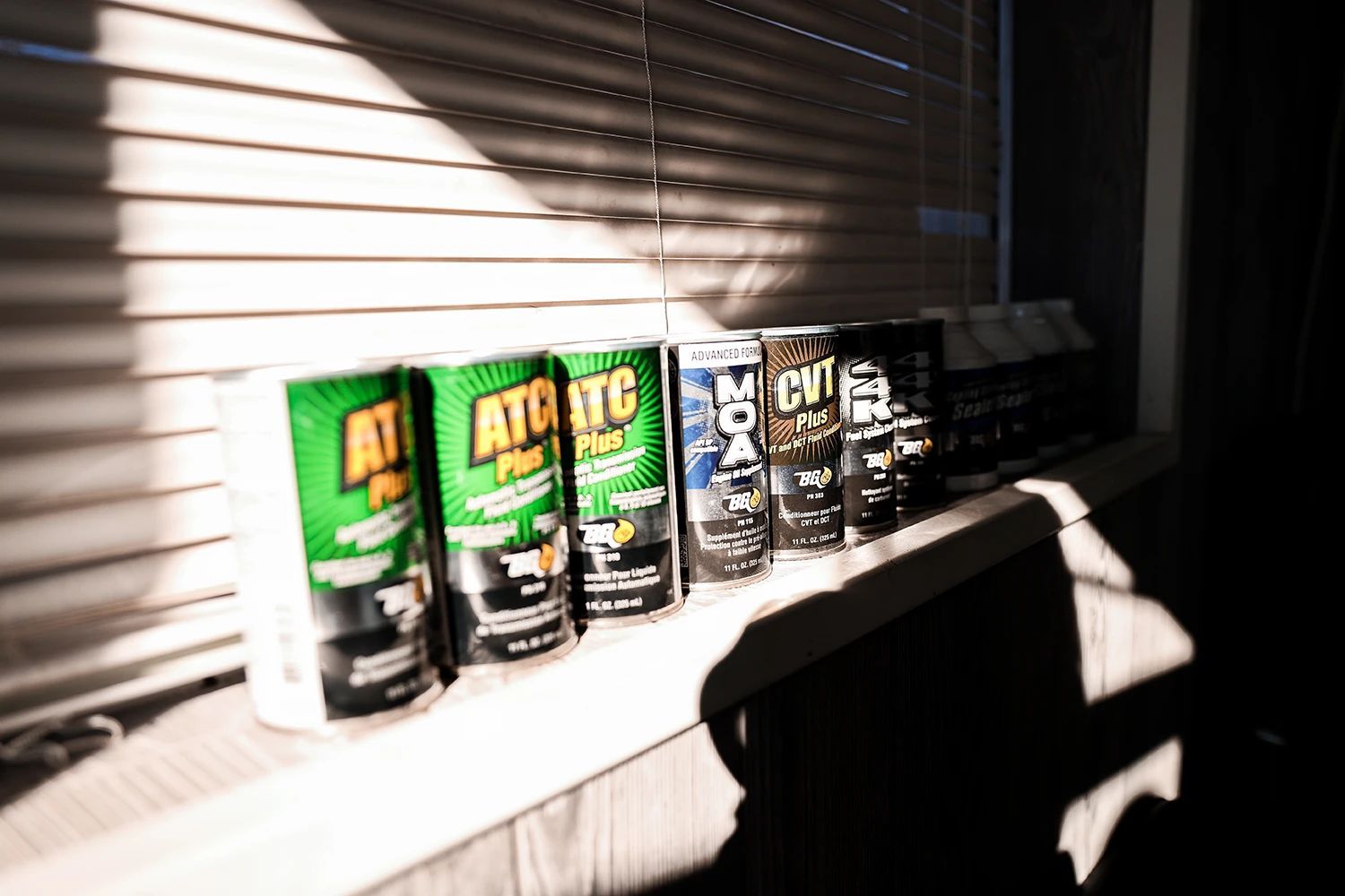 Row of supplement containers on a windowsill, illuminated by sunlight through blinds | Kaiser Automotive