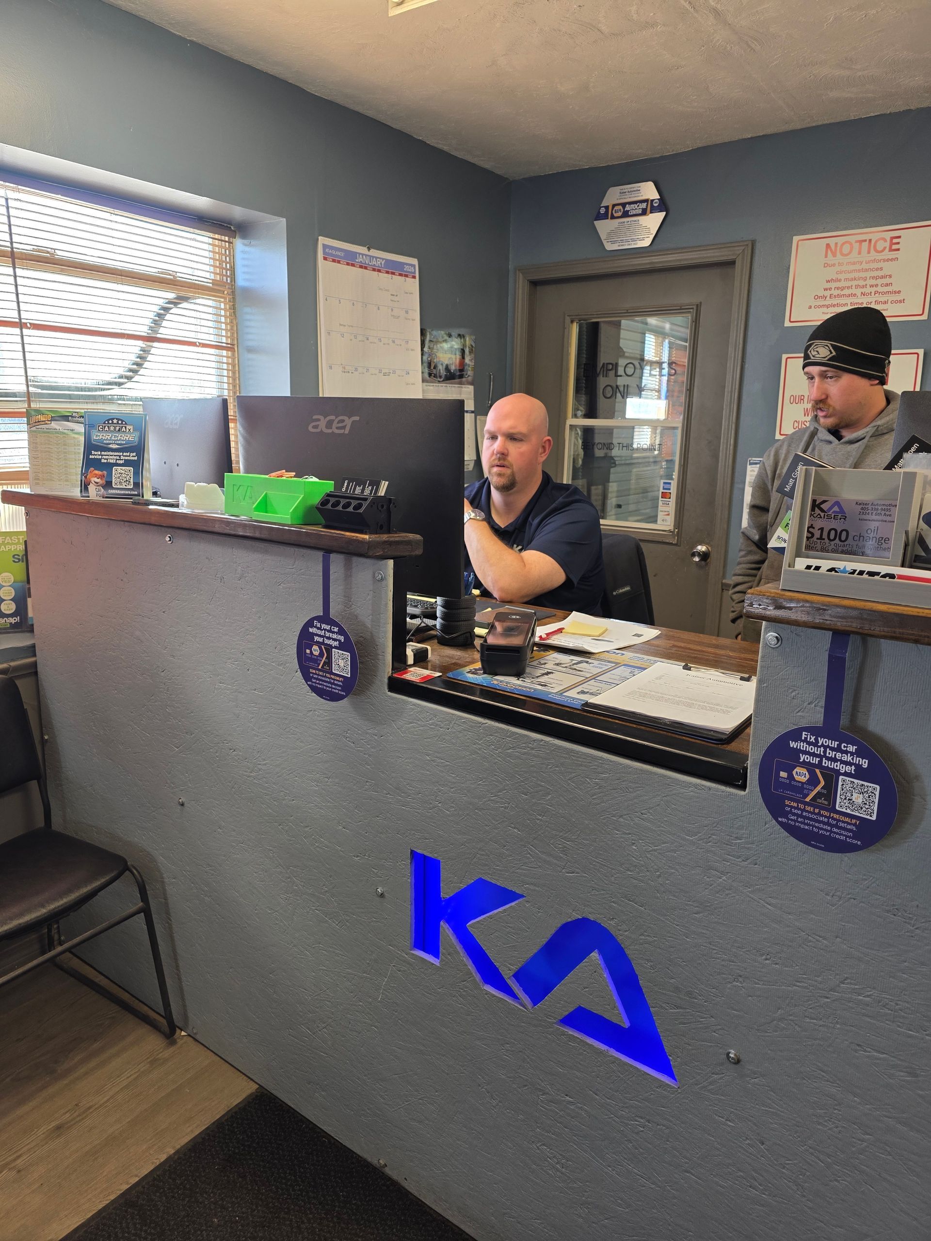 Two men at a car repair shop front desk. One looks at a computer, another in a beanie stands beside him | Kaiser Automotive Tire & Alignment