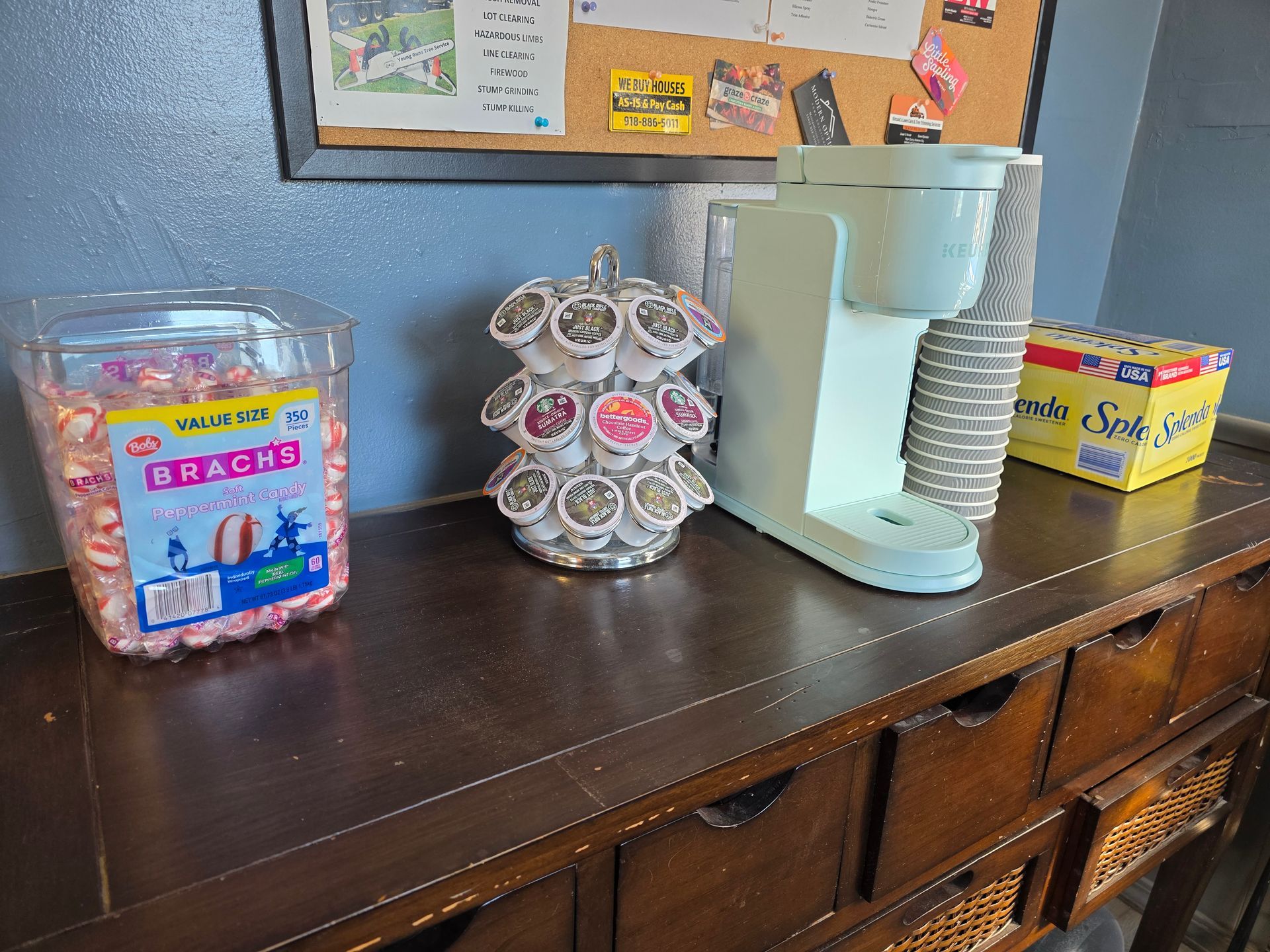 Coffee station with coffee maker, K-cups, candy, and a box of stir sticks on a wooden cabinet | Kaiser Automotive Tire & Alignment