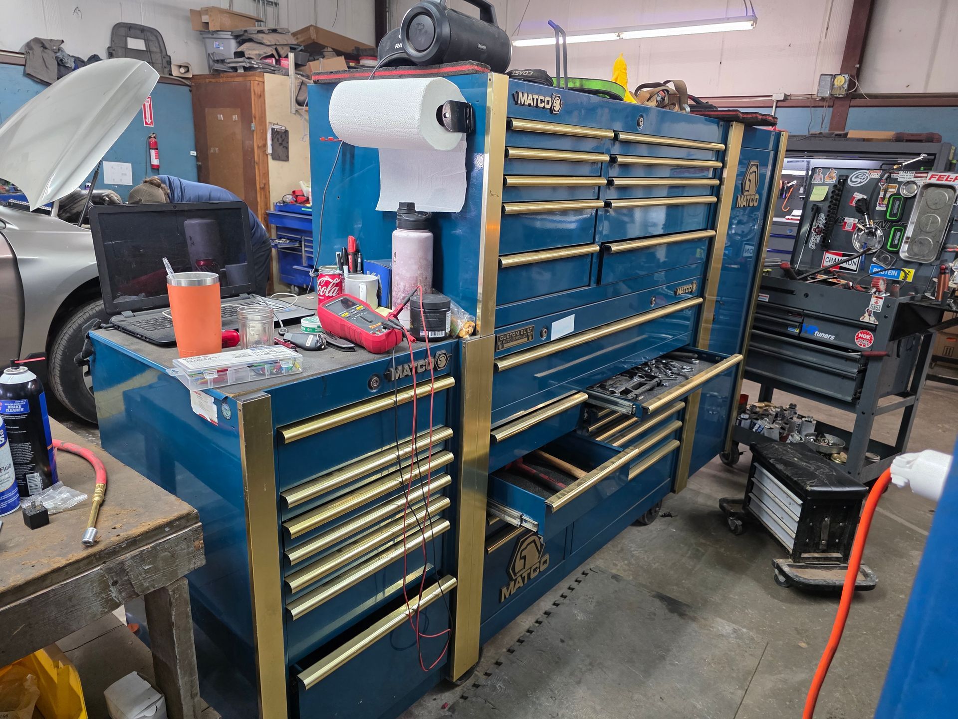 Blue tool chest in a cluttered garage, with gold trim and various items on top | Kaiser Automotive Tire & Alignment