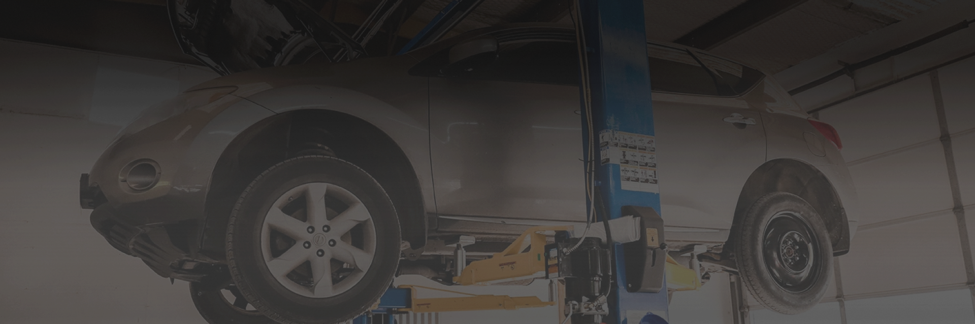 A silver car lifted by a hydraulic lift in a garage for inspection or repair.