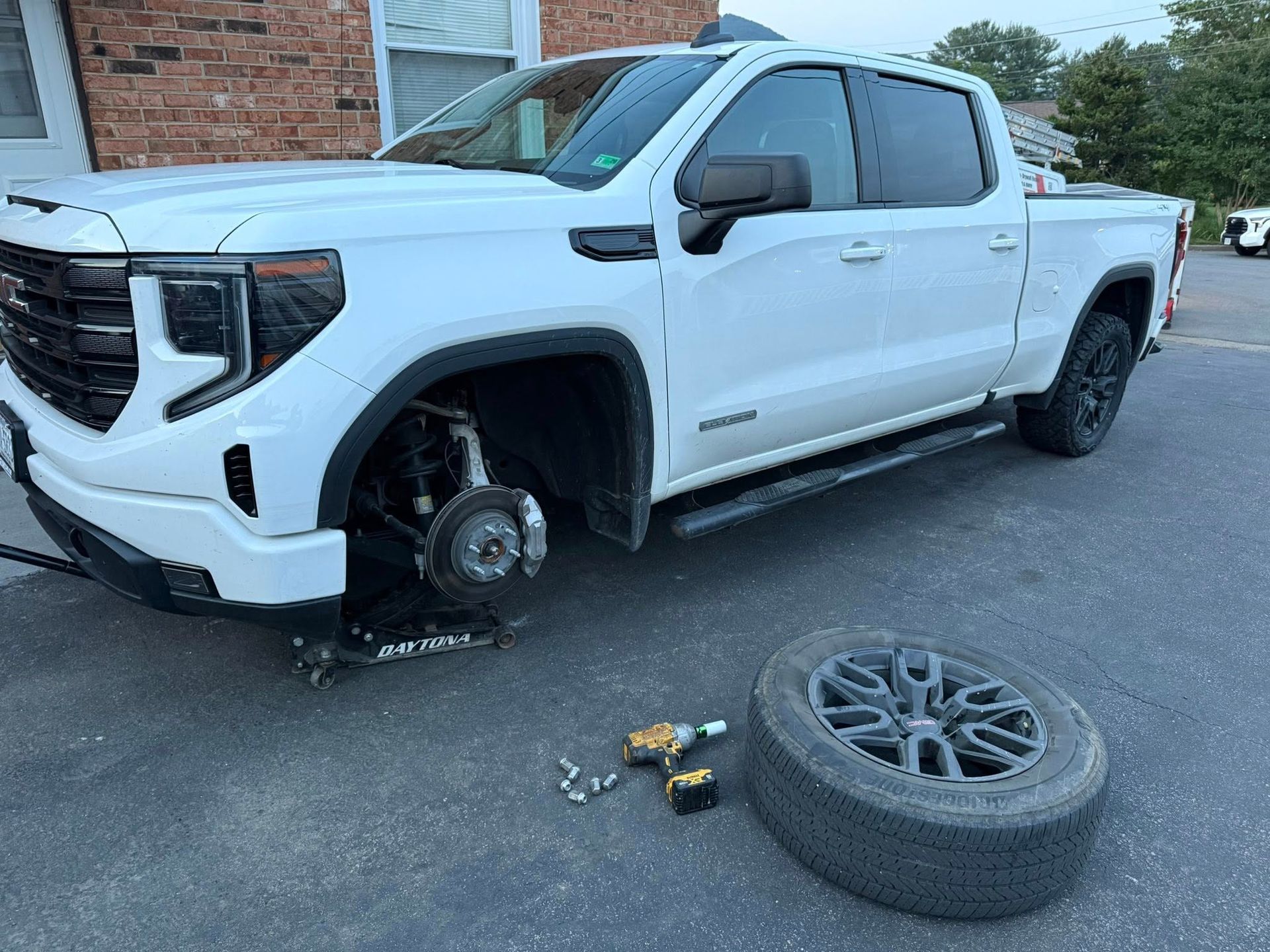A white truck with its tires missing is parked in front of a brick building.