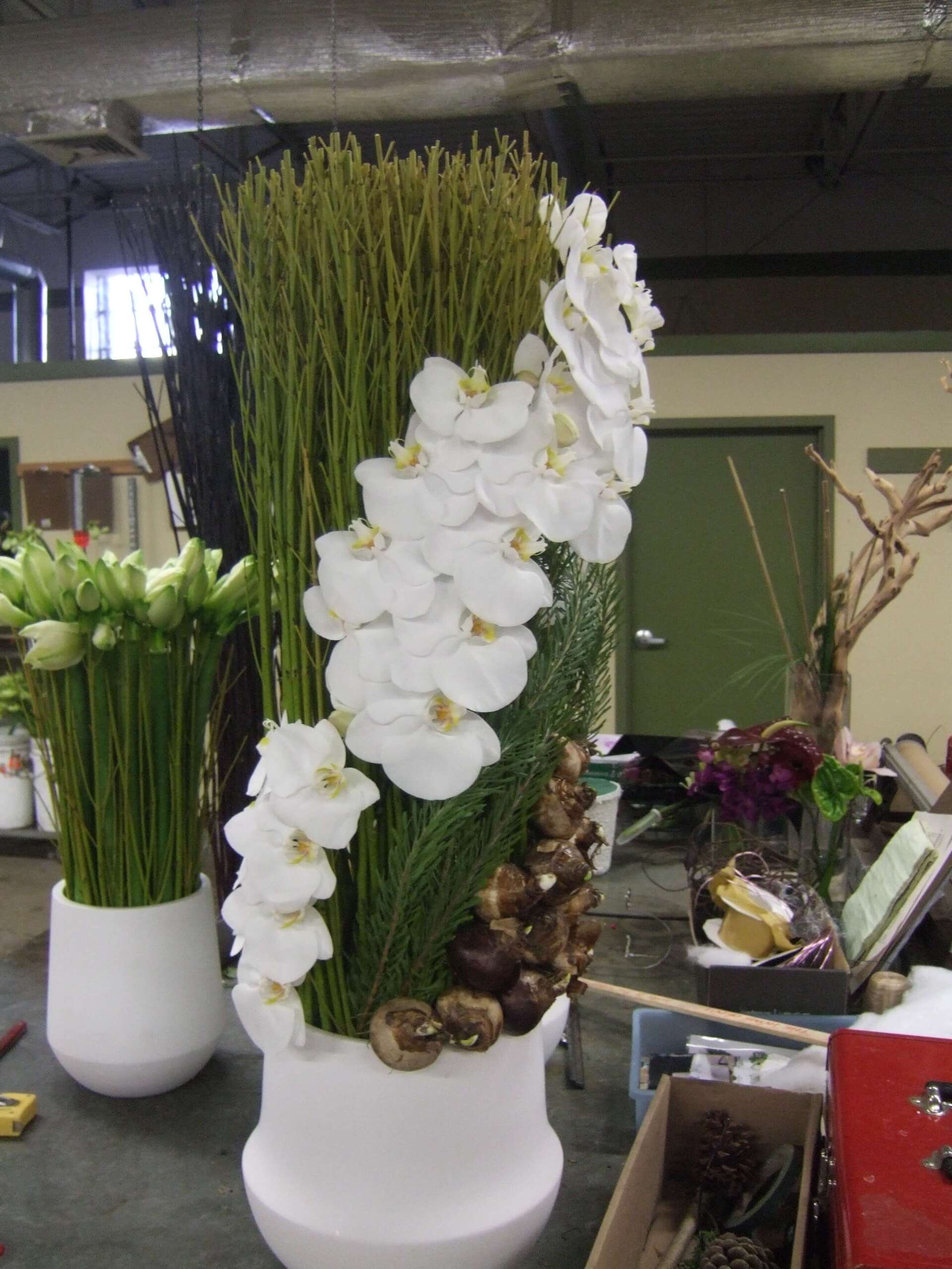 A white vase filled with white flowers and greenery - flowers designed by Flowers by Leo