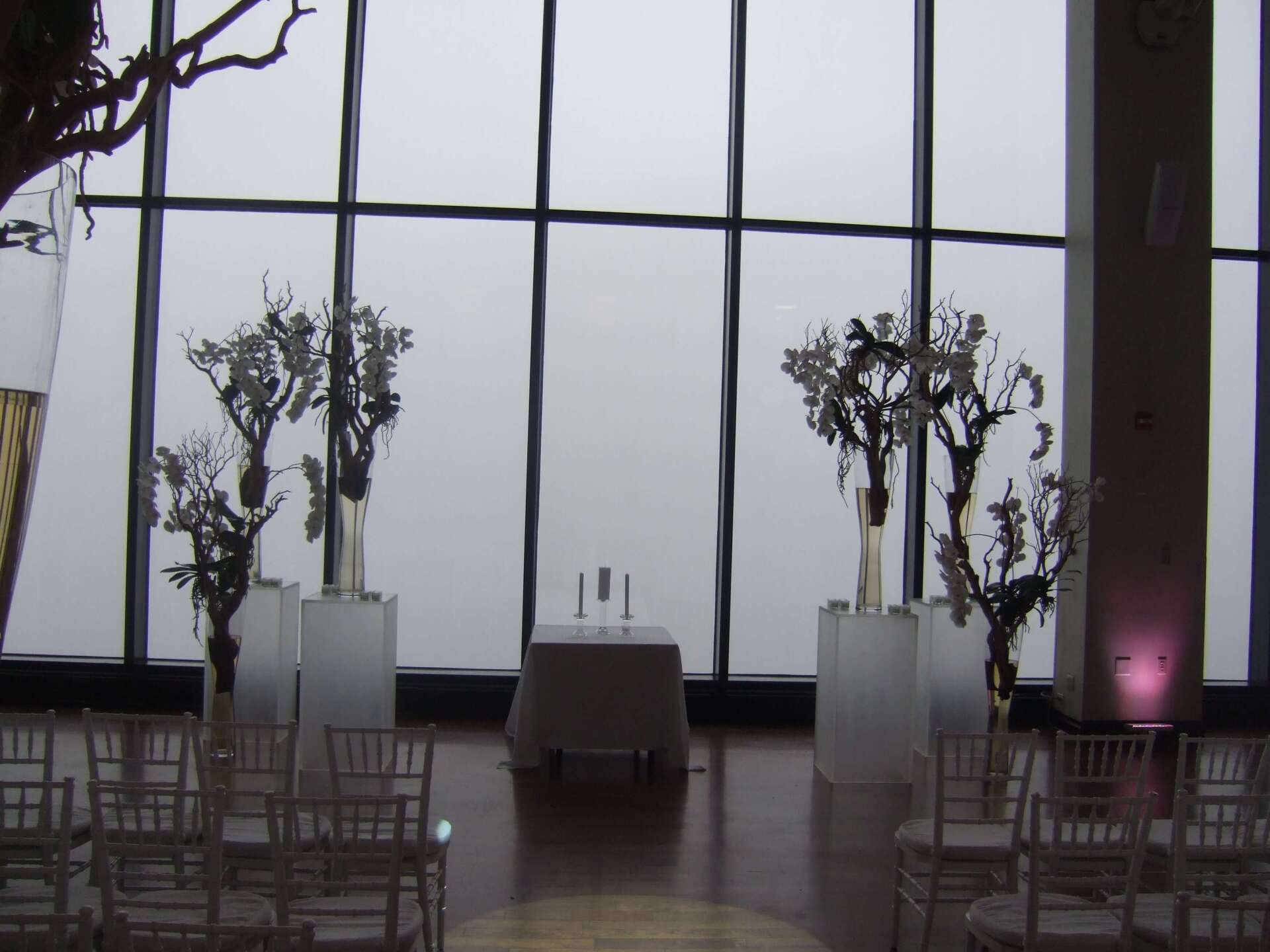 A room with a table and chairs in front of a large window - flowers designed by Flowers by Leo