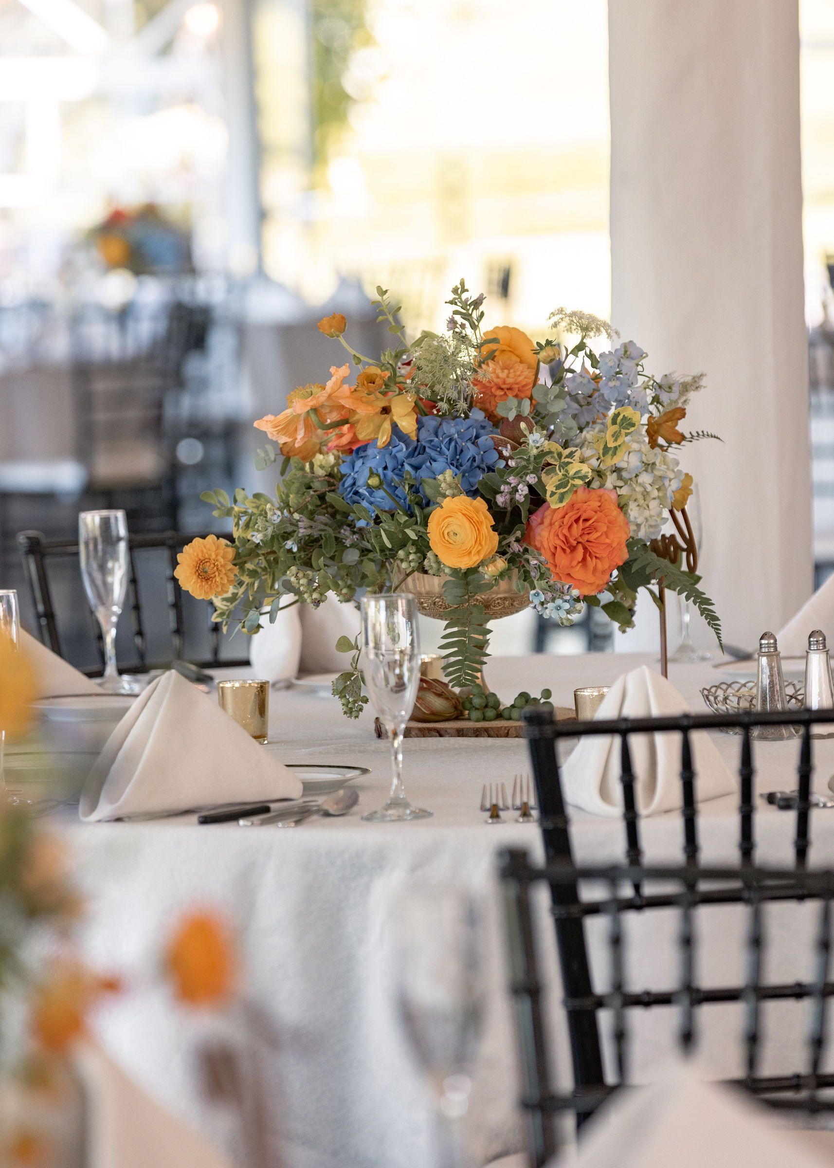 A table set for a wedding reception with a vase of flowers on it - flowers designed by Flowers by Leo.