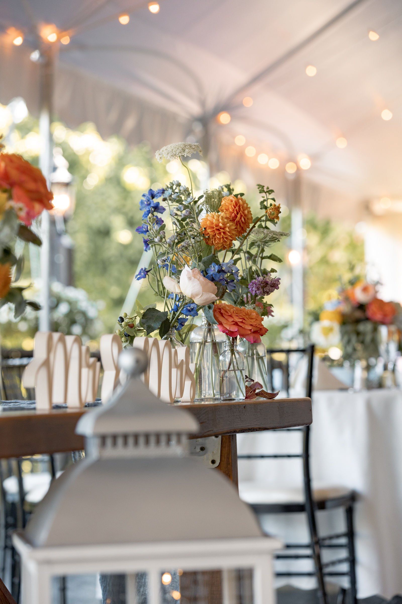 A table with a vase of flowers on it and a lantern on it - flowers designed by Flowers by Leo.