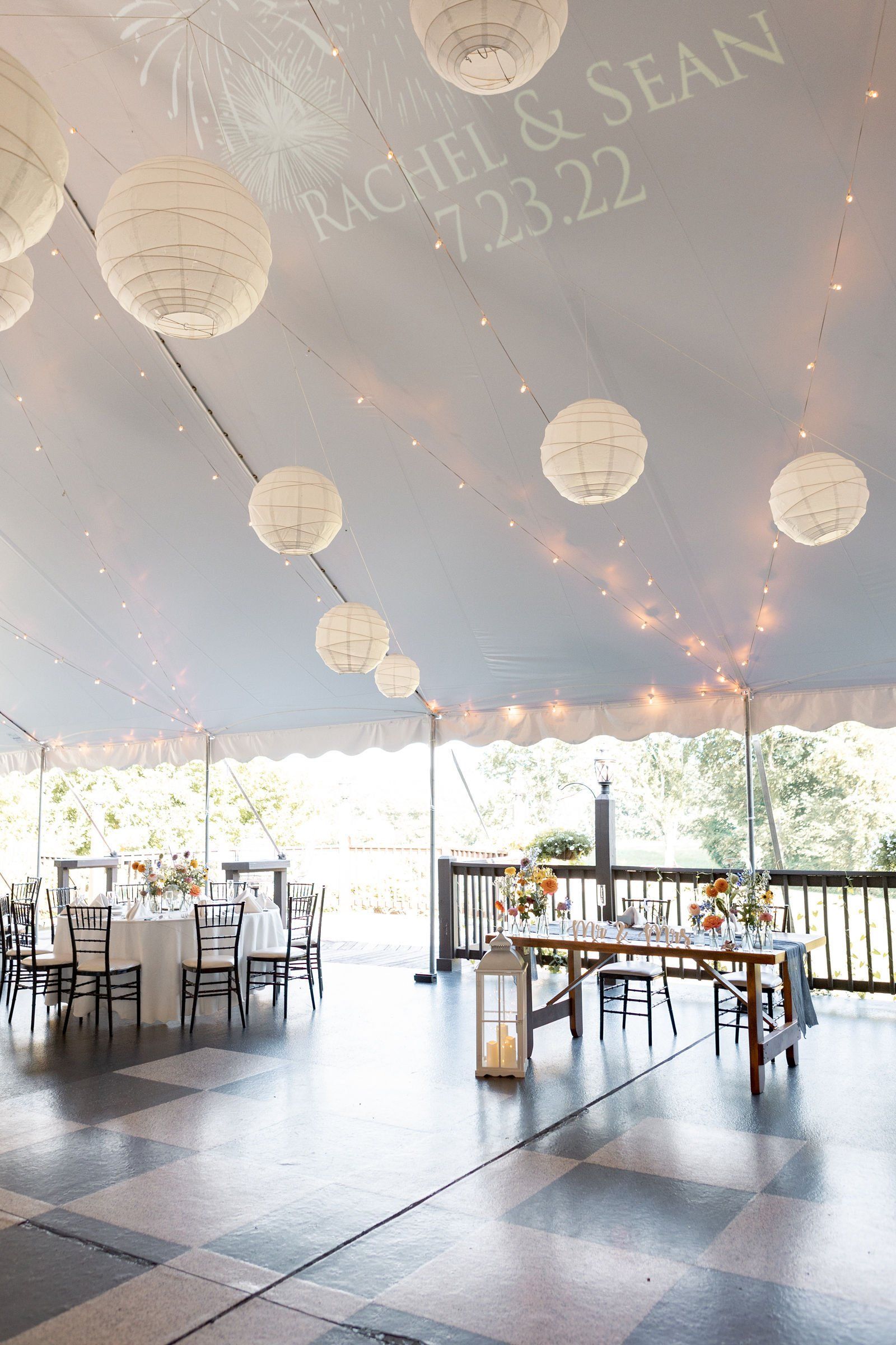 A large room with tables and chairs under a tent - flowers designed by Flowers by Leo