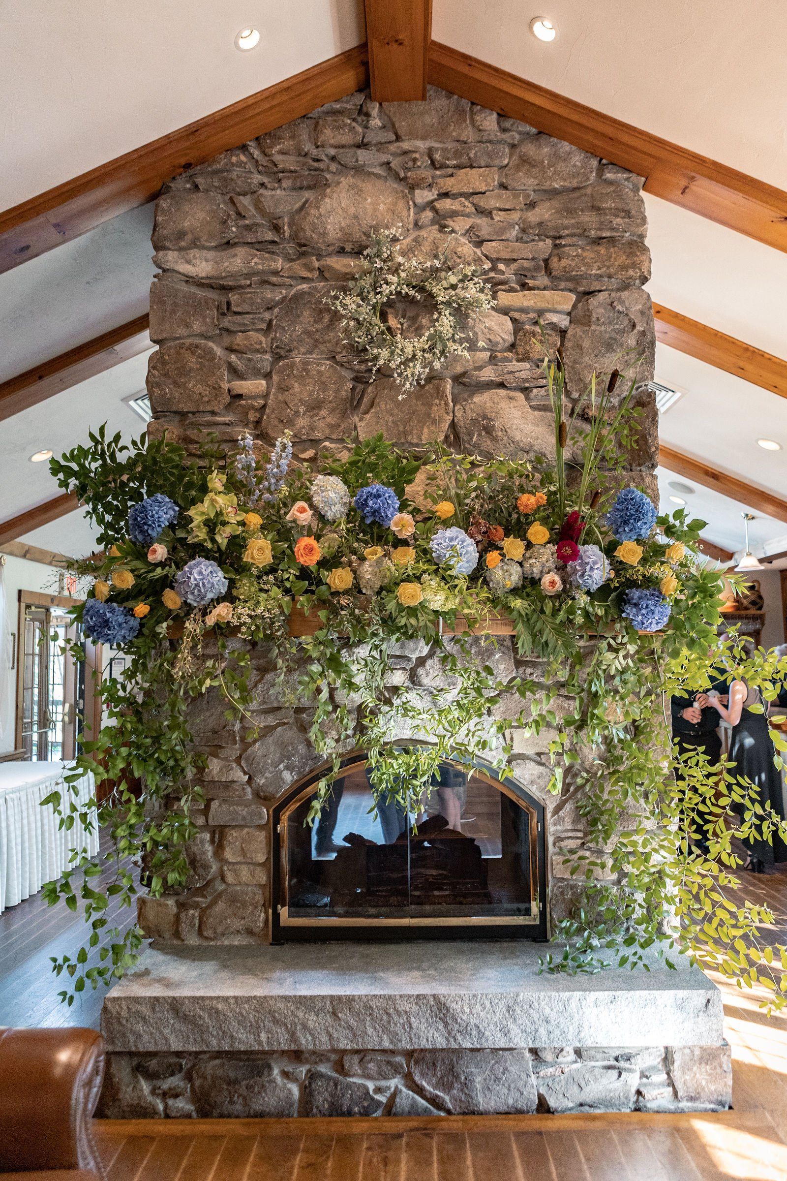 A stone fireplace decorated with flowers in a living room - flowers designed by Flowers by Leo.
