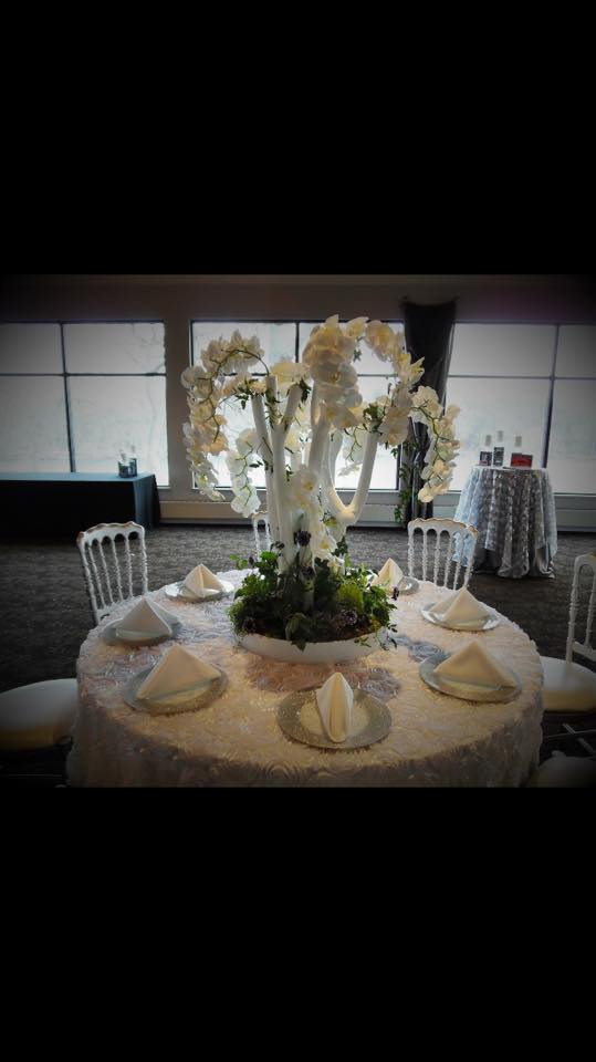 A table with a vase of flowers on it is set for a wedding reception - flowers designed by Flowers by Leo.