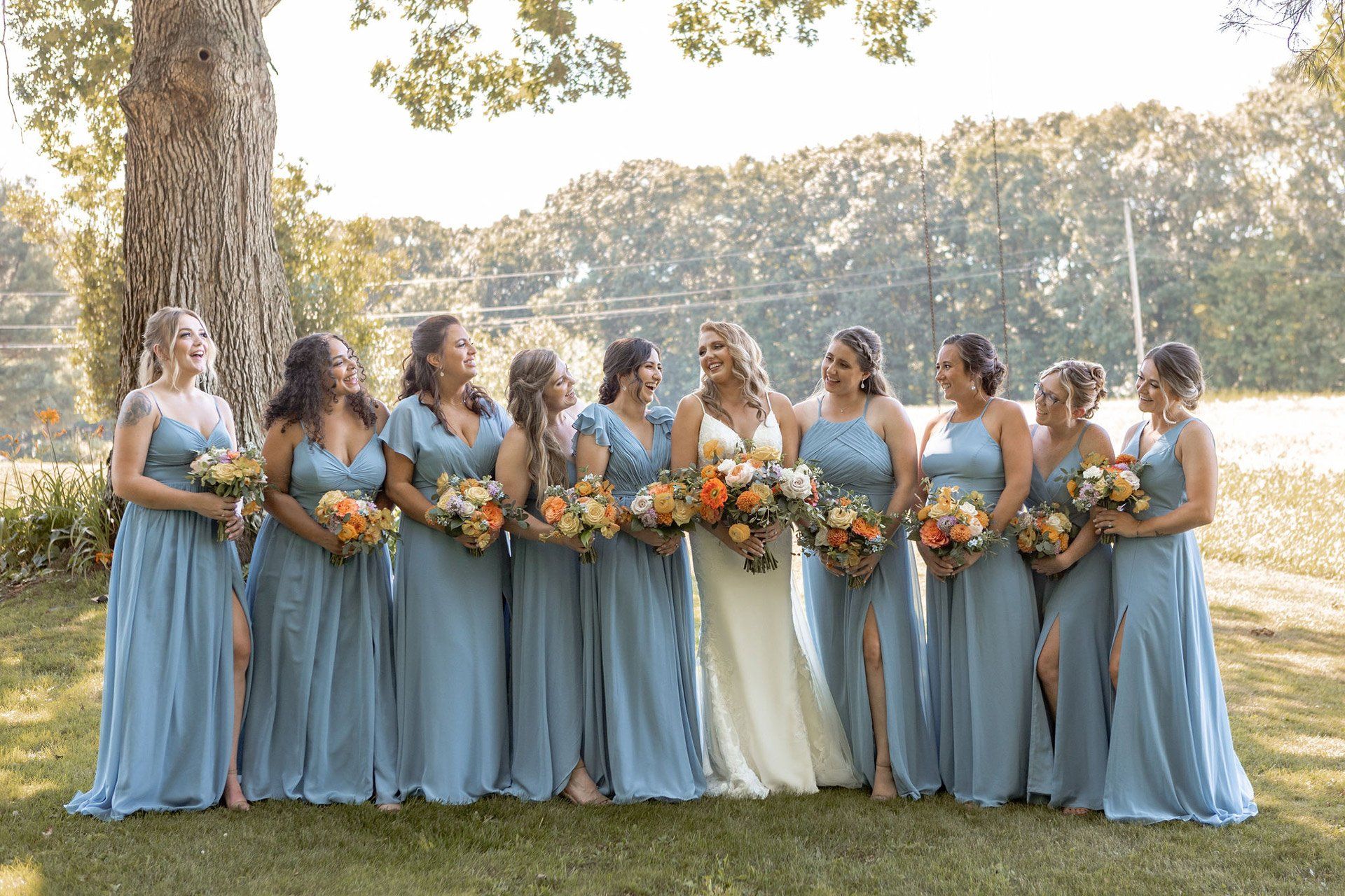 A bride and her bridesmaids are posing for a picture in front of a tree - flowers designed by Flowers by Leo.