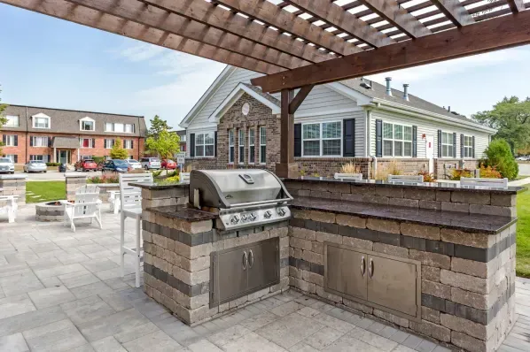 a grill is sitting under a pergola on a patio in front of a house .