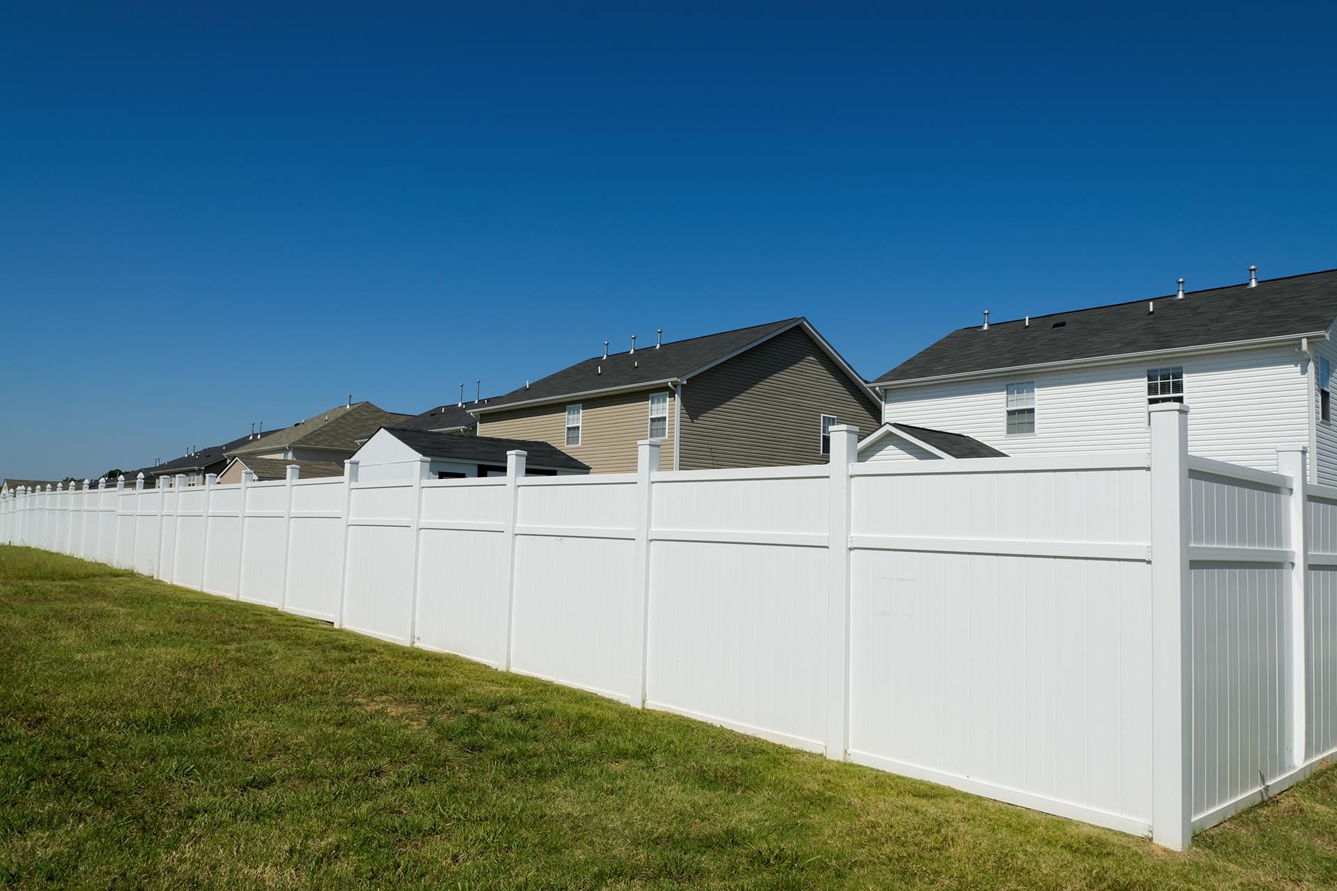a white fence surrounds a lush green field in front of a row of houses .