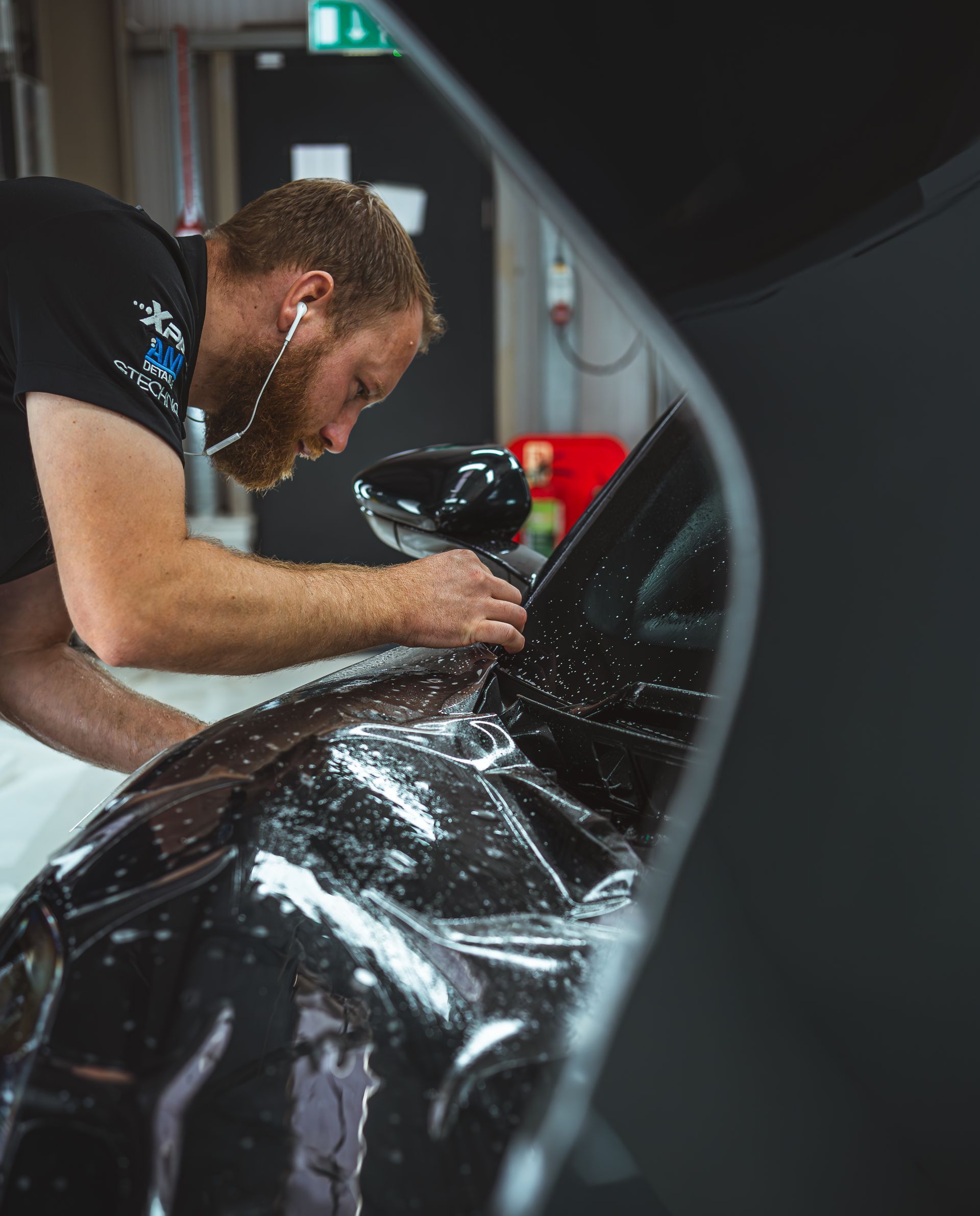 A man is wrapping a car with Paint Protection Film in a garage.