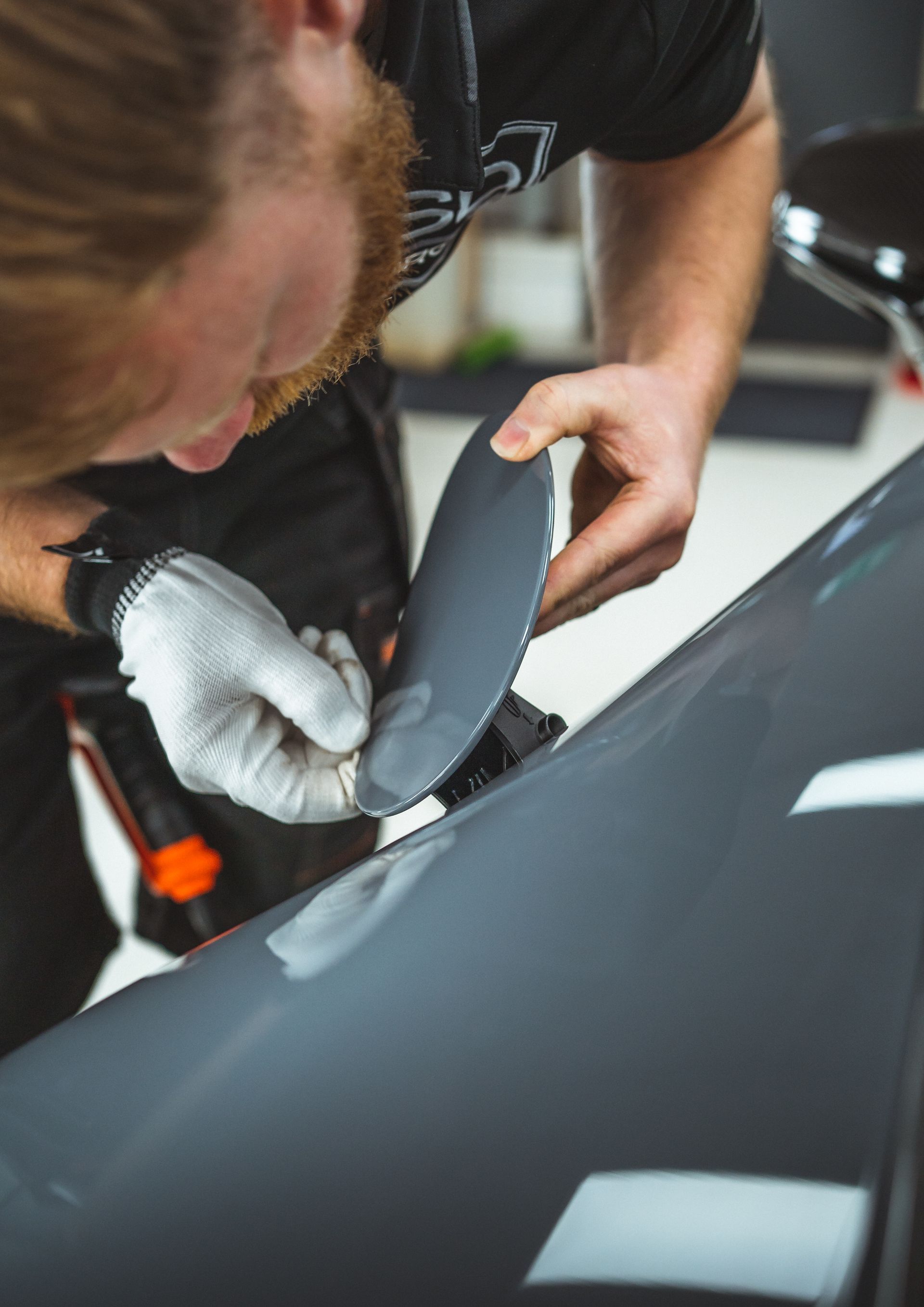 A man is installing PPF on a grey car.