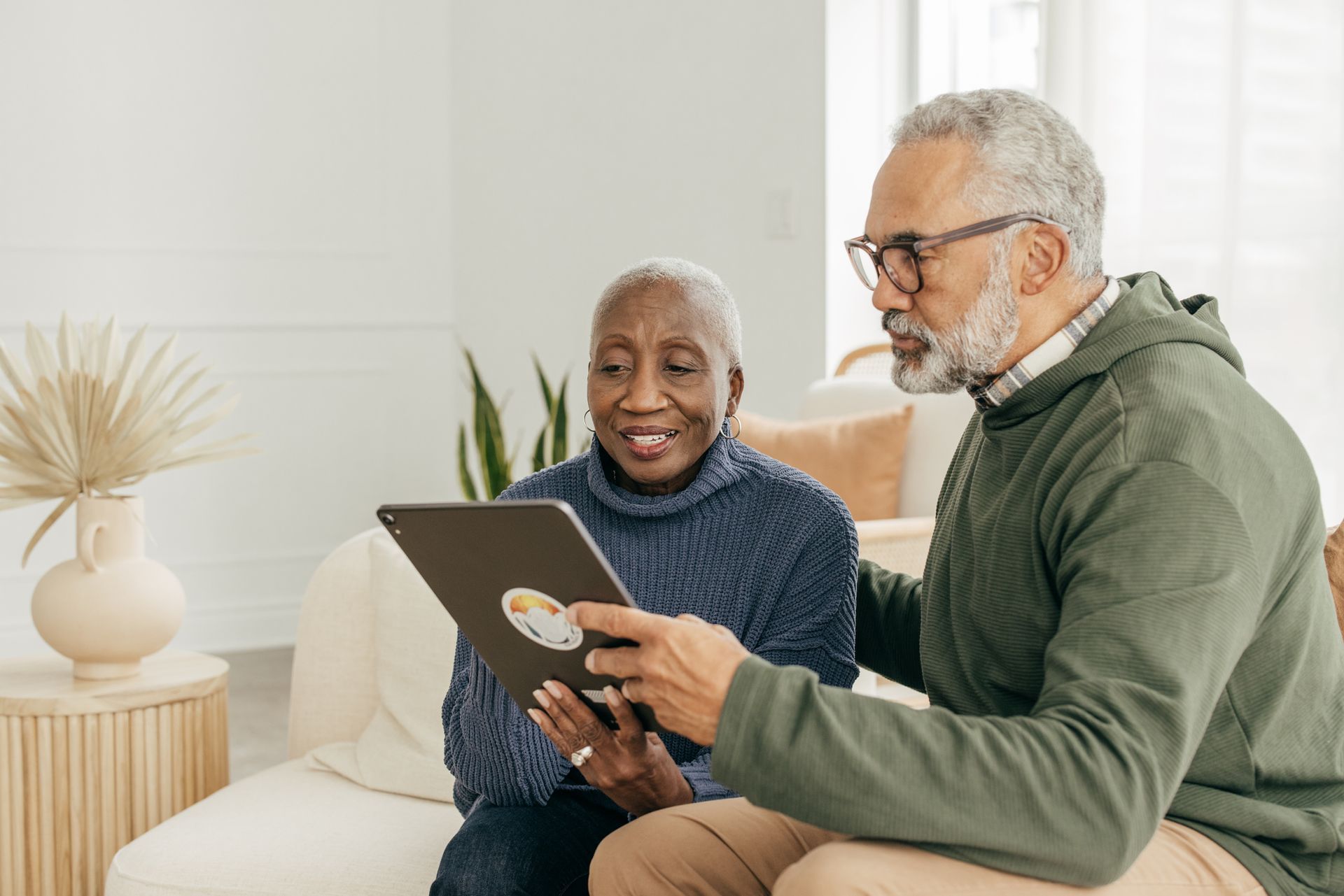 A man and a woman are sitting on a couch looking at a tablet.