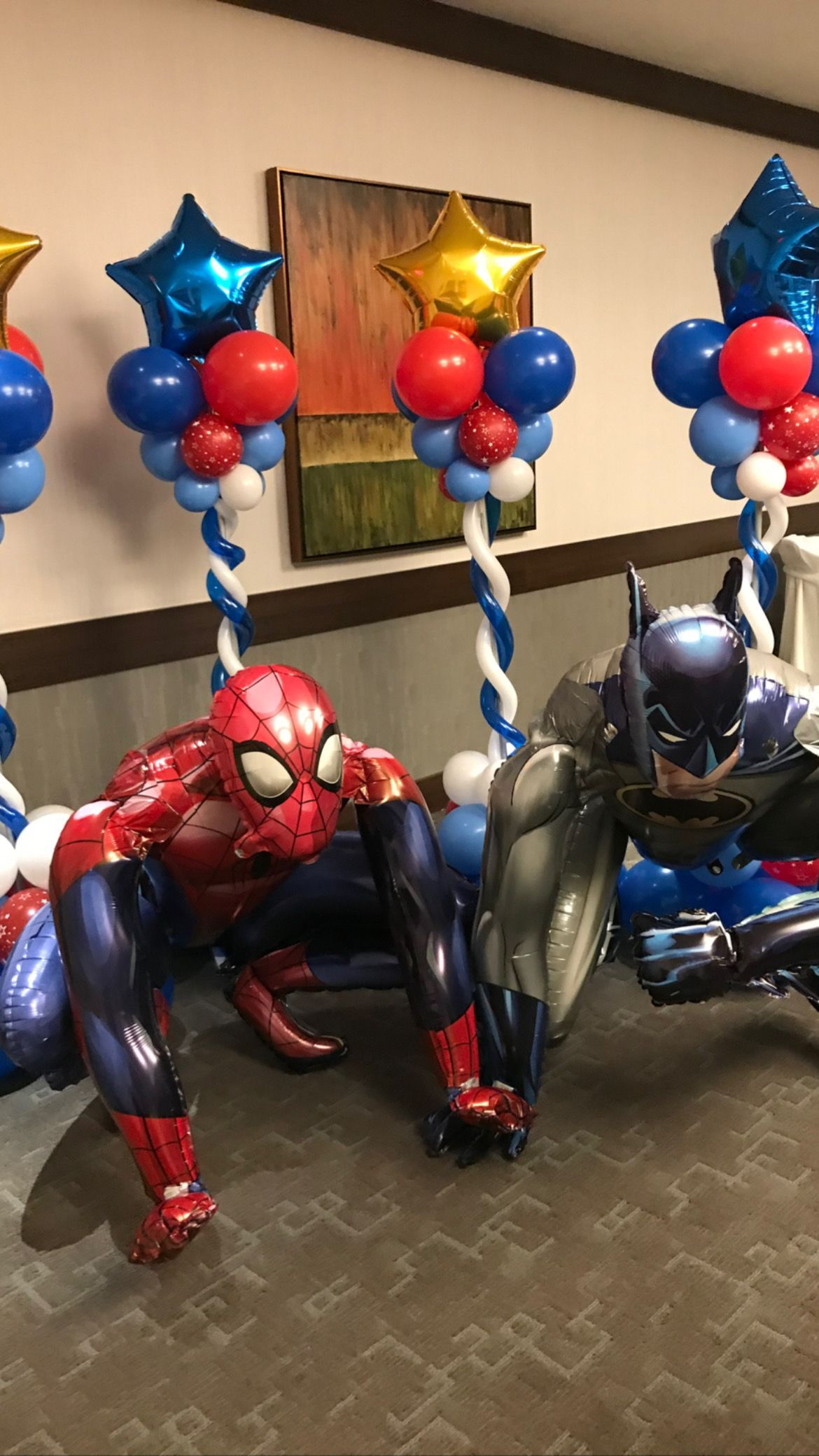 Spiderman and batman balloons are sitting next to each other in a room.