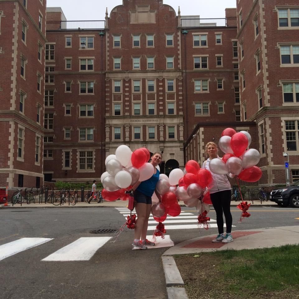 Two women holding balloons in front of a large brick building