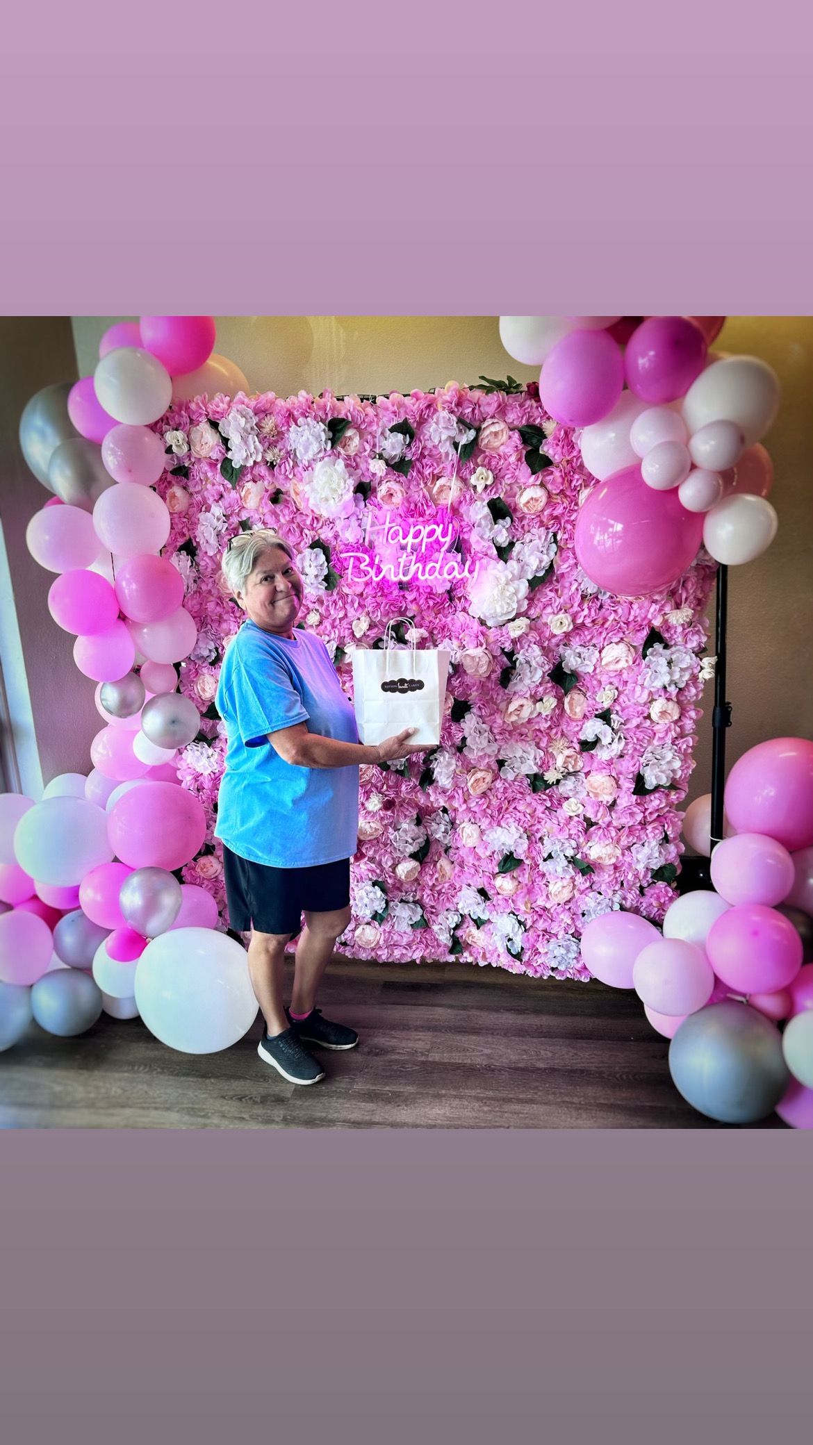 A man is standing in front of a pink flower wall holding a cake.