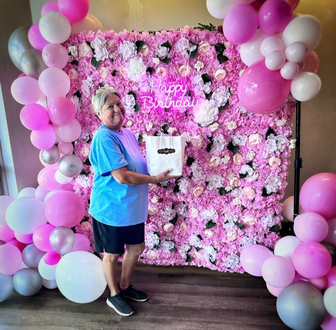 A man is standing in front of a pink flower wall holding a cake.