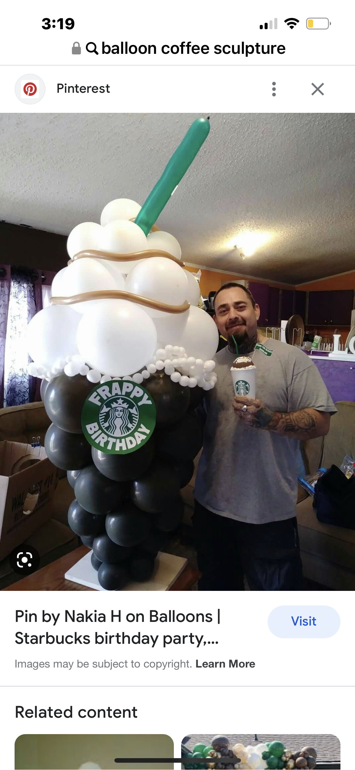 A man is standing next to a giant starbucks drink made out of balloons.