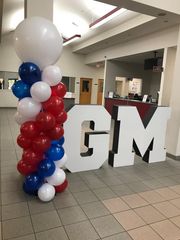 A large gm sign is surrounded by red white and blue balloons