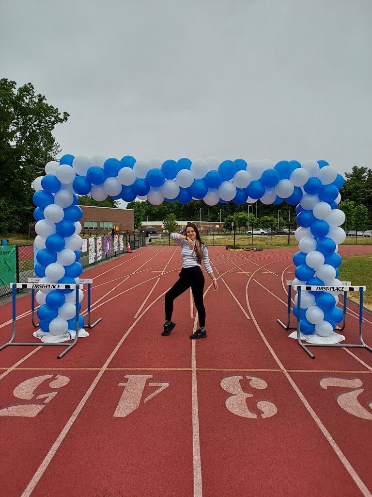 A woman is standing on a track surrounded by blue and white balloons.