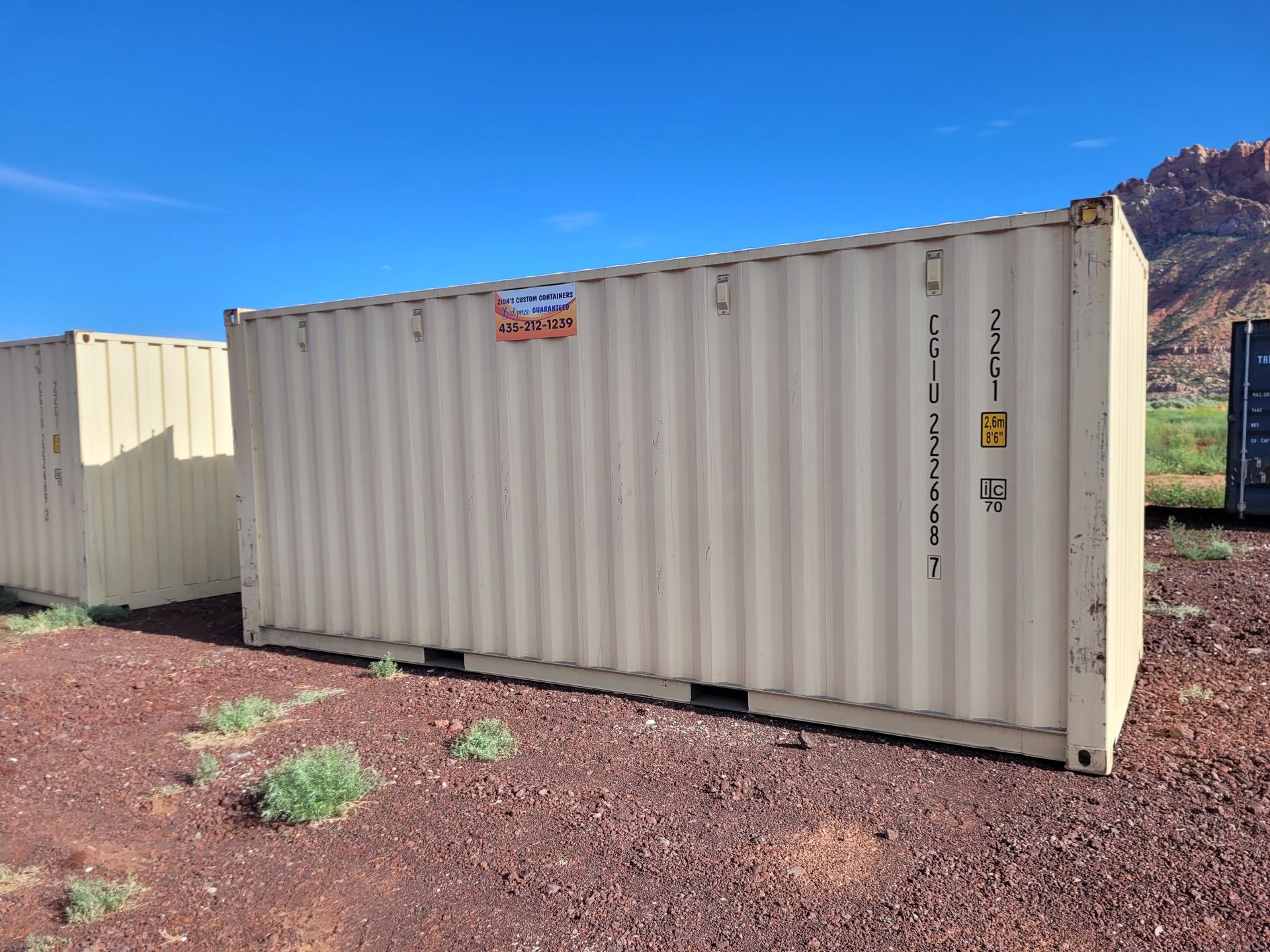 Two shipping containers are sitting on top of a dirt field.