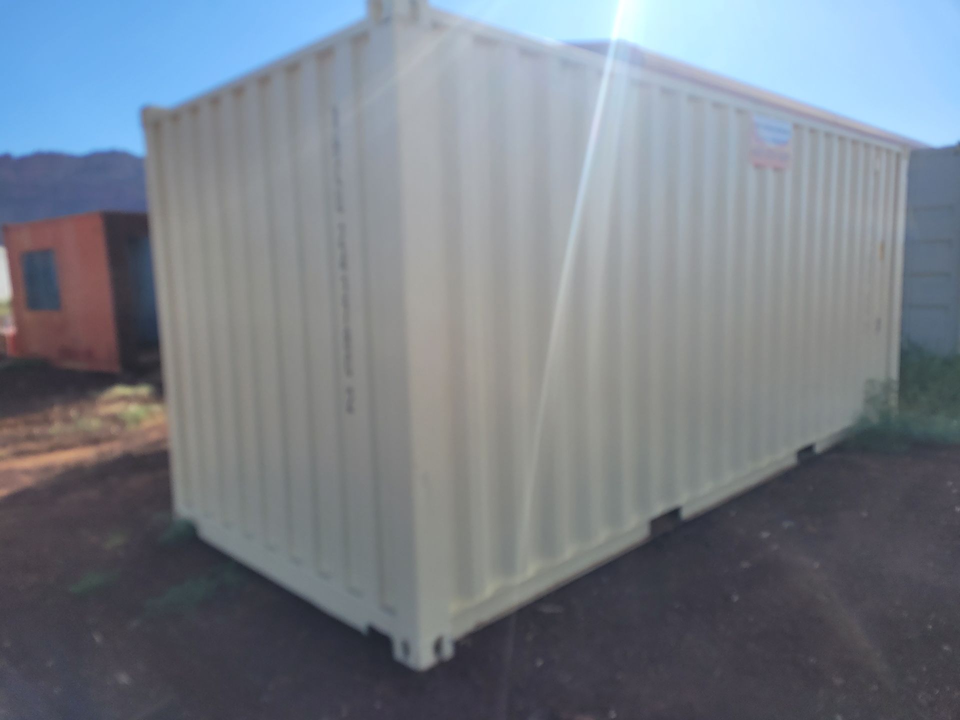 A white shipping container is sitting on top of a dirt road.