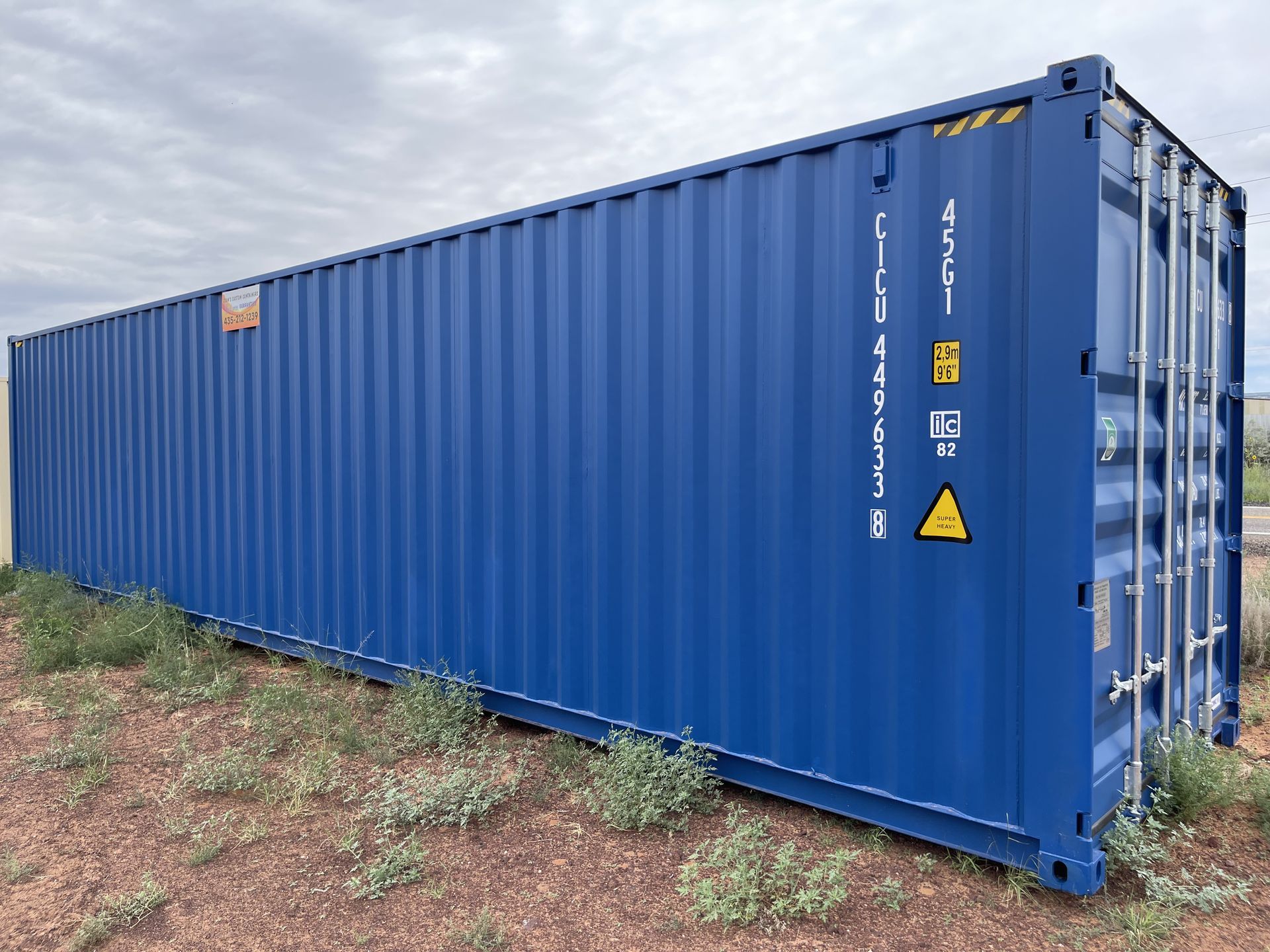 A large blue shipping container is sitting on top of a dirt field.