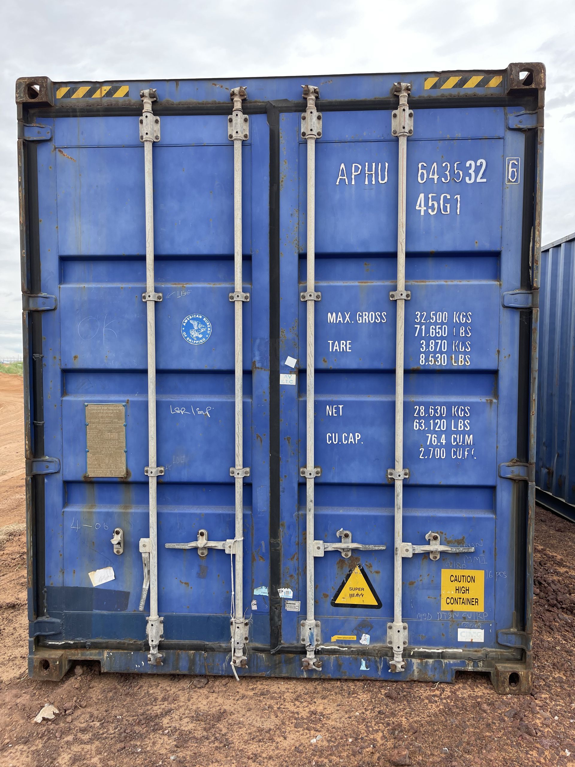 A blue shipping container is sitting on top of a dirt field.