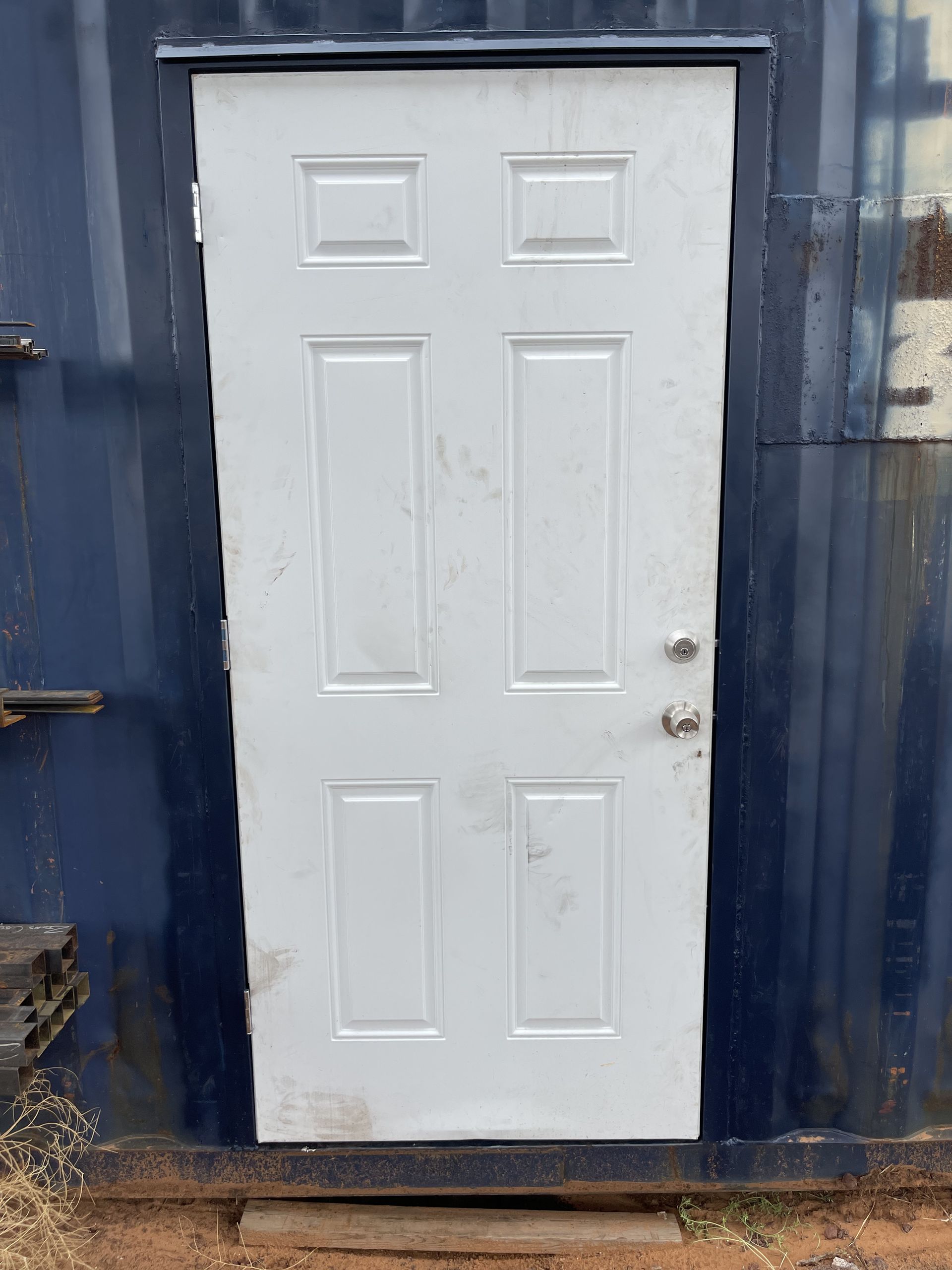 A white door is sitting in front of a blue building.