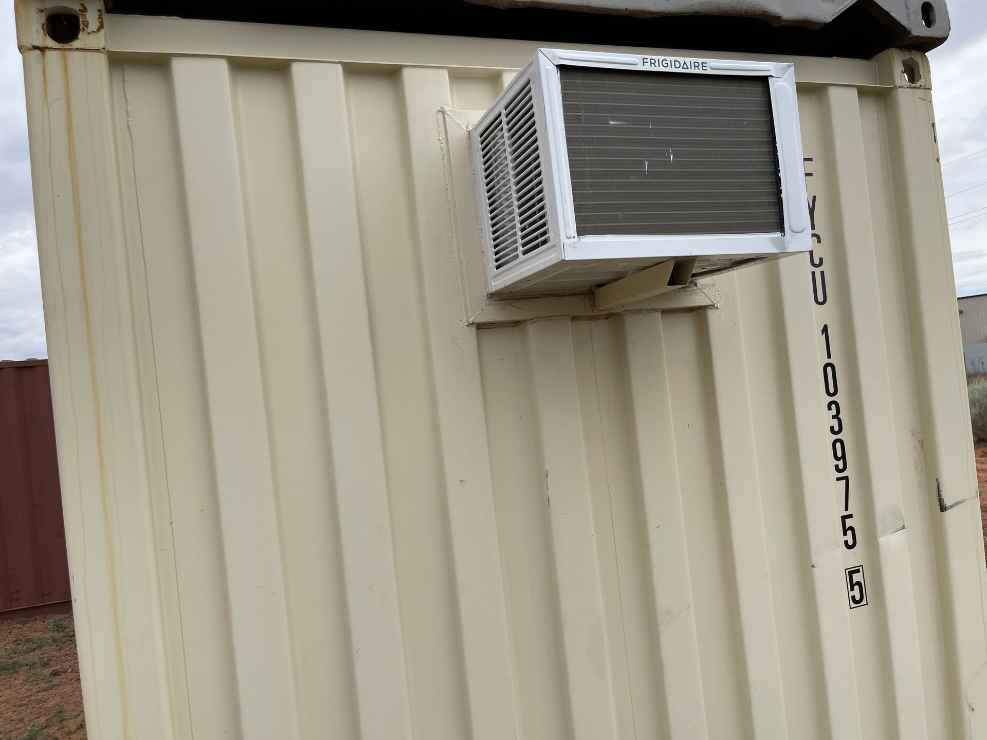 A small air conditioner is mounted on the side of a shipping container.