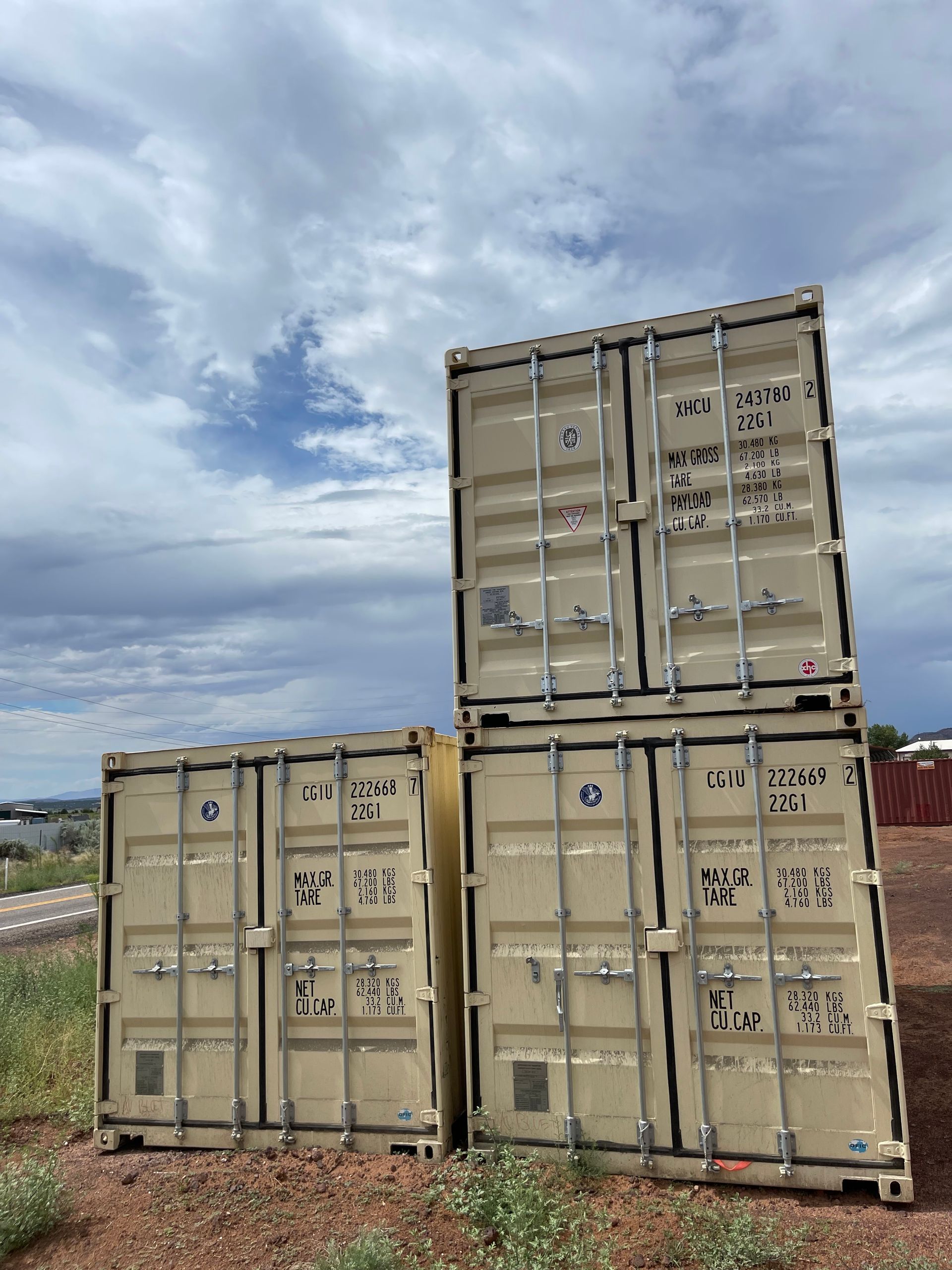 Three shipping containers are stacked on top of each other in a field.