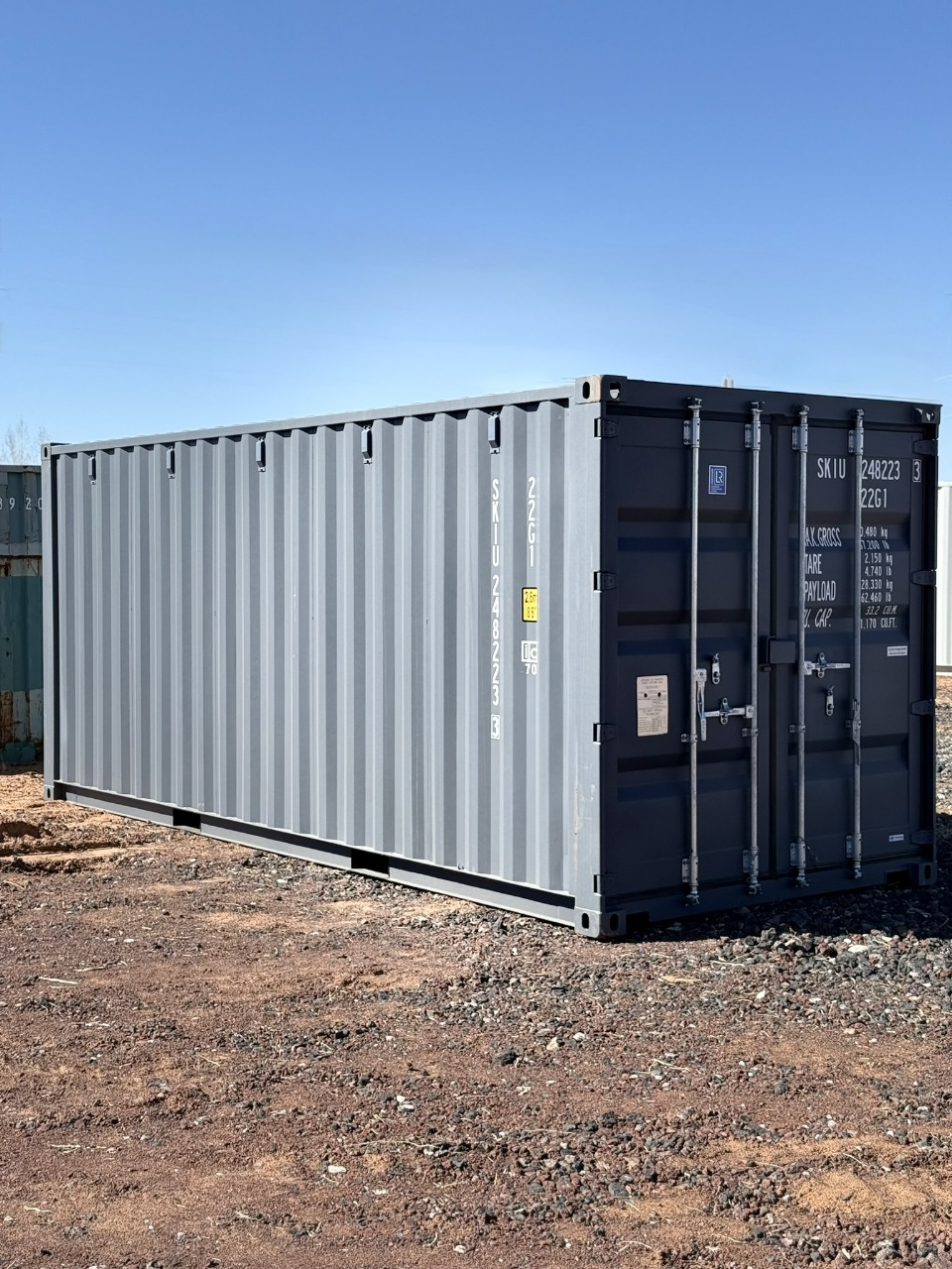 A large gray shipping container is parked in a dirt field.
