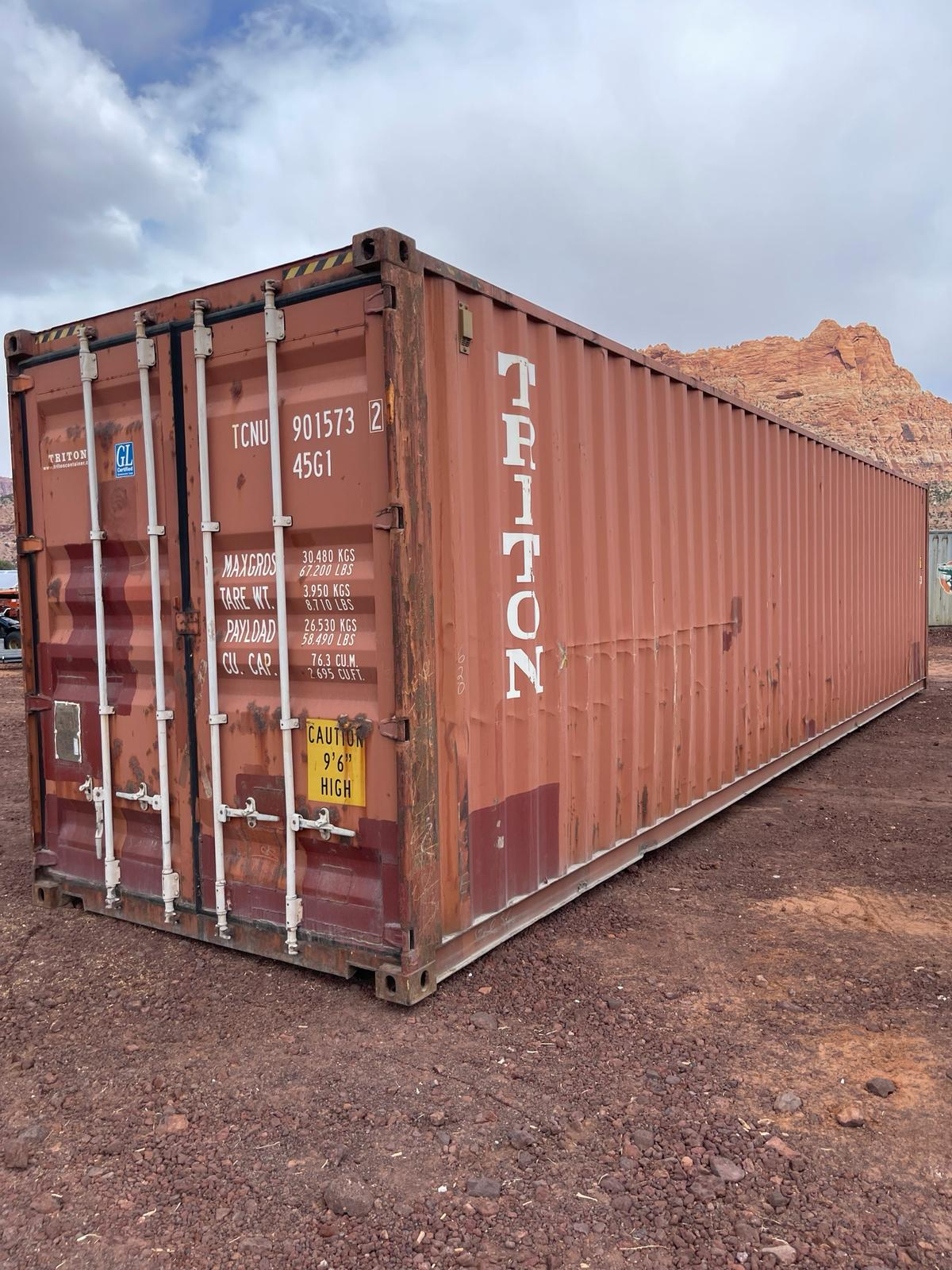 A red shipping container is sitting on top of a dirt field.