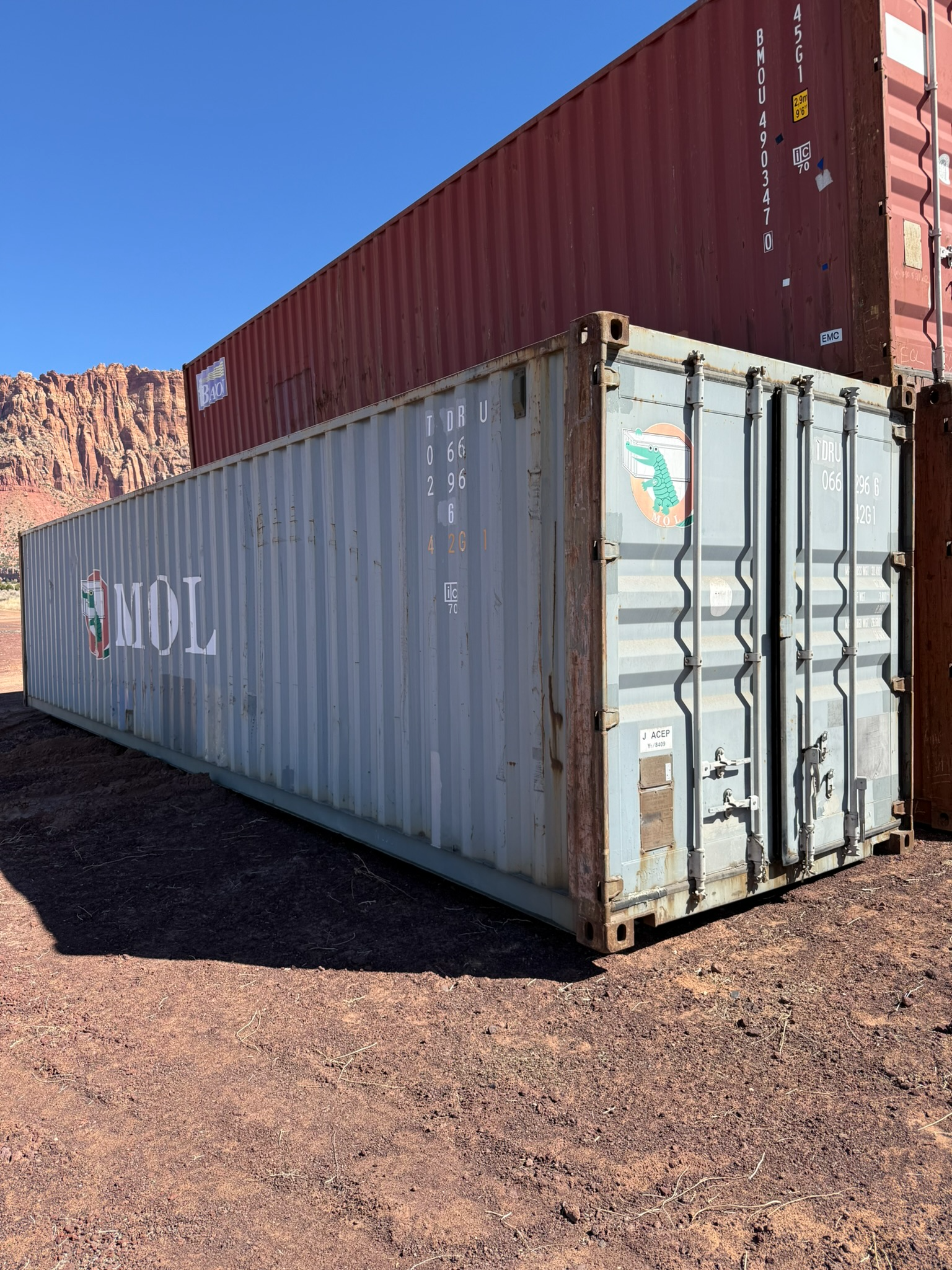 A large shipping container is sitting on top of a dirt field.