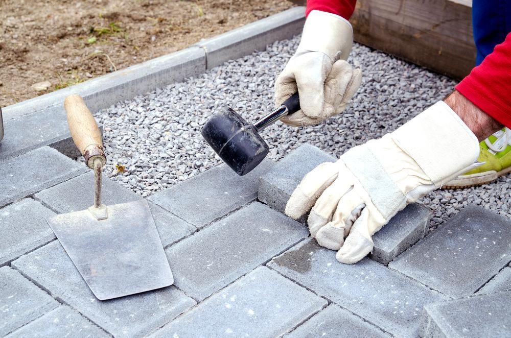 A Person Is Laying Bricks on A Sidewalk with A Mallet and Trowel — S & L Sand & Gravel in Evans Head, NSW