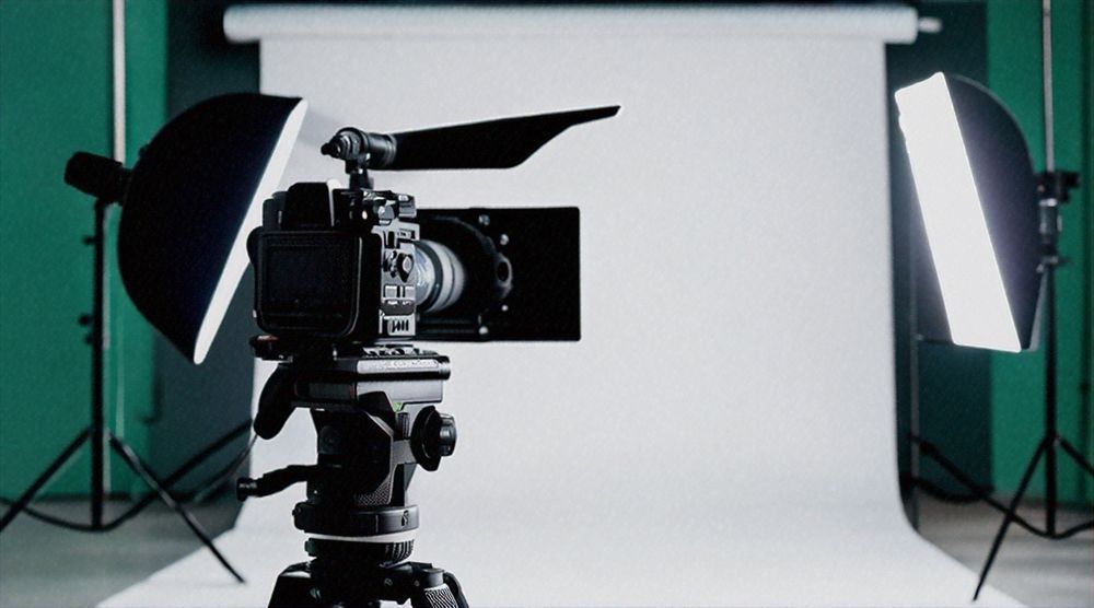 Video camera on tripod in a studio with two softbox lights and a white backdrop