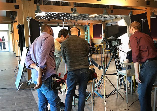 People gathered around a camera setup in a studio, adjusting equipment on tripods and cables.