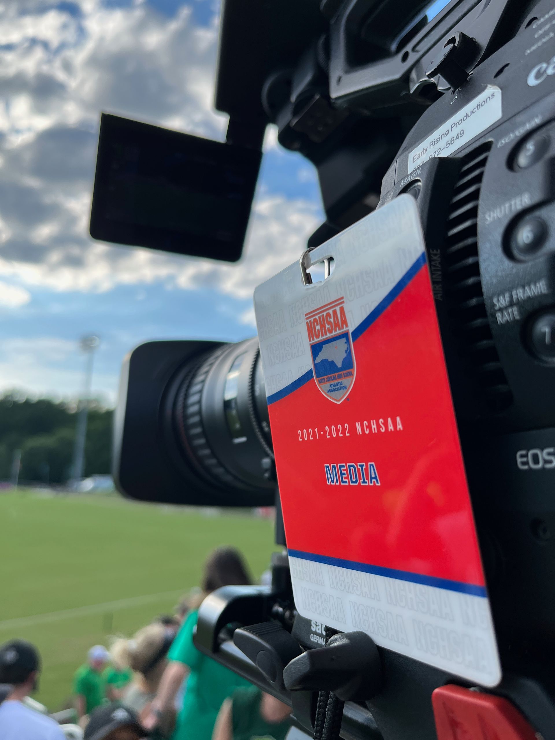 Close-up of a soccer broadcast camera with a red and blue sideline sticker on a field